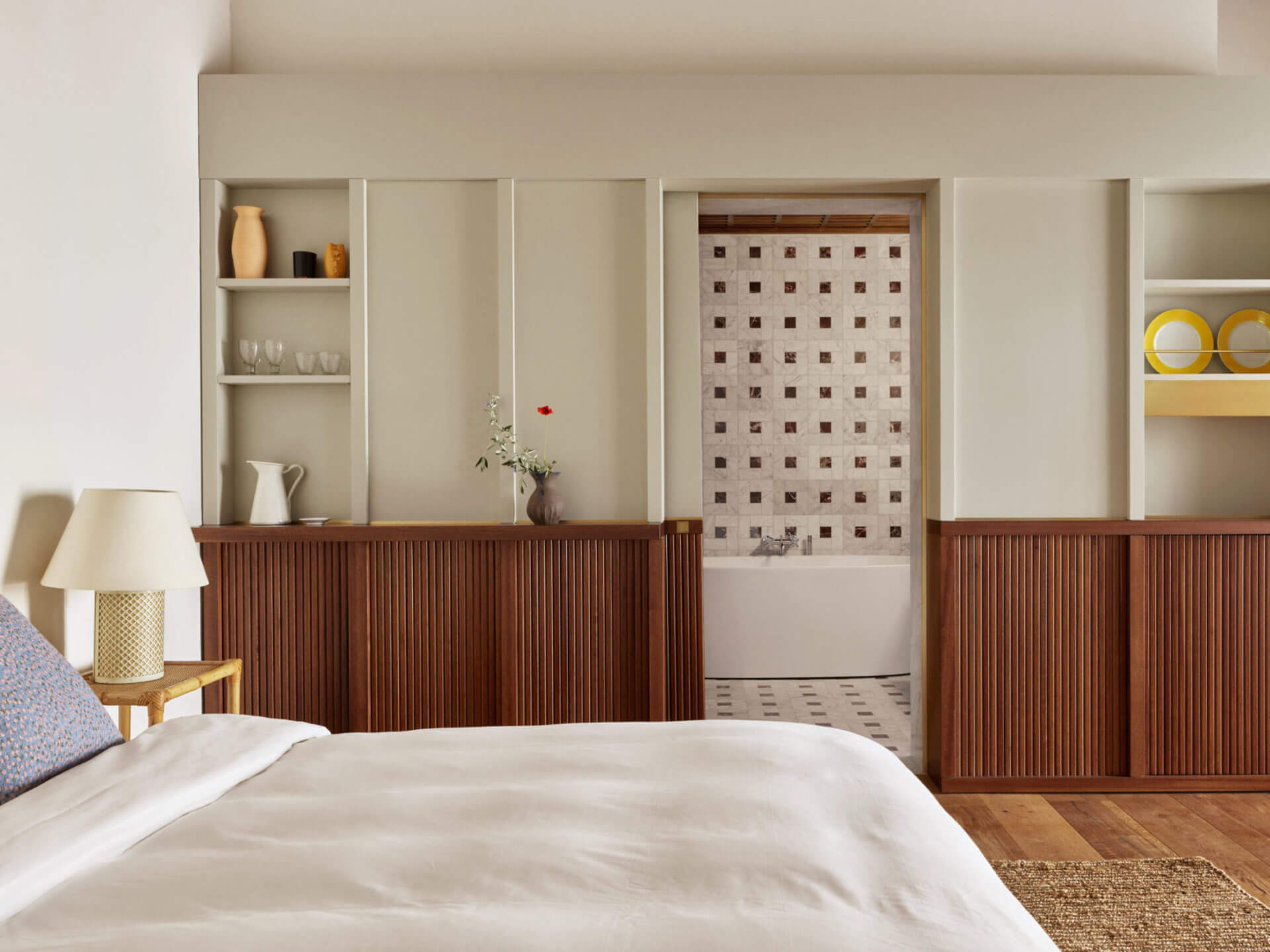 Villa Lena, Europe — Mid-century modern bedroom with walnut-paneled headboard, cream bedding, built-in shelving, and ensuite bathroom visible through open doorway.
