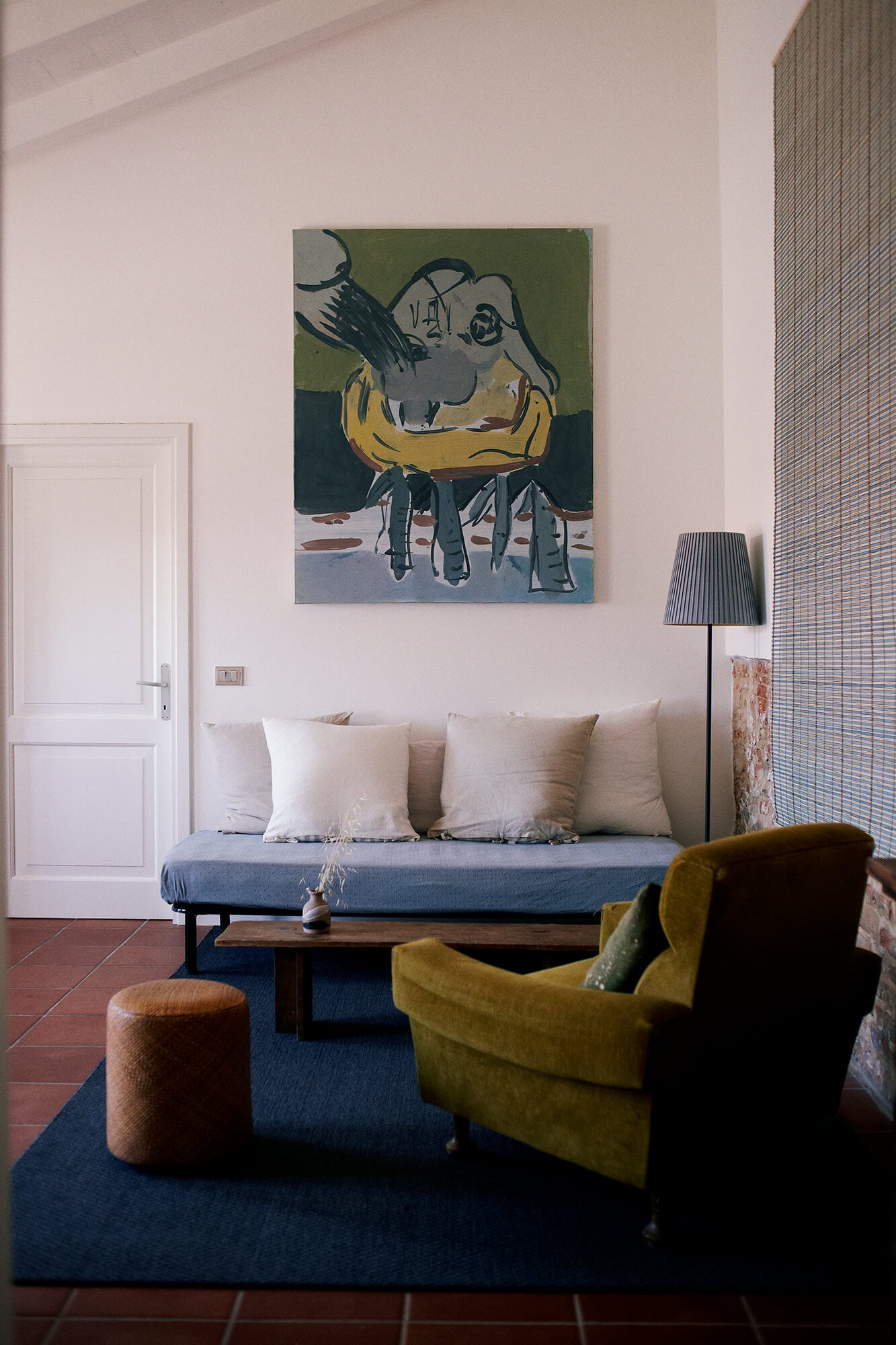Villa Lena, Europe — Modernist living room with olive armchair, blue daybed, artwork, floor lamp, and terracotta tile flooring.