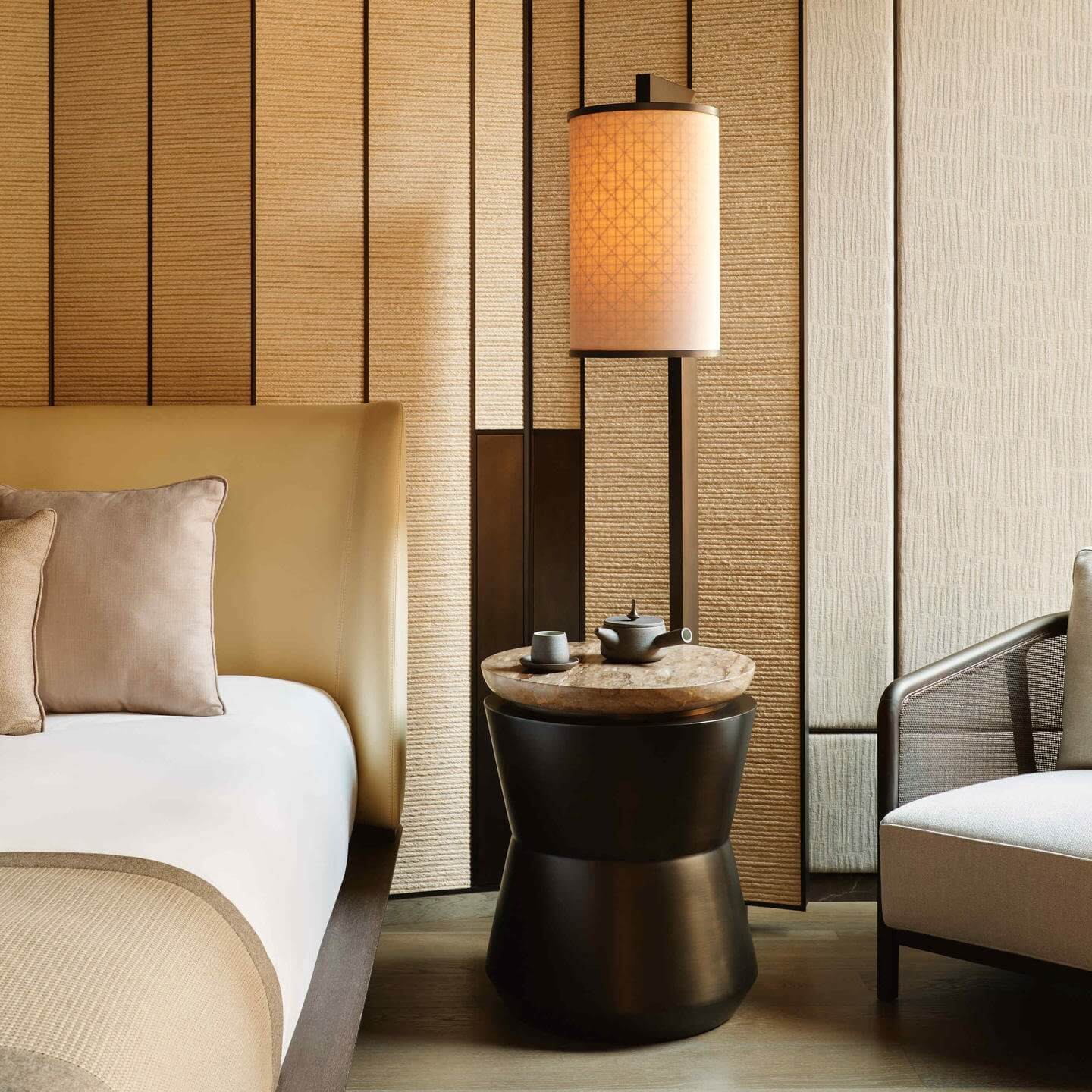 Aman New York, New York, United States — Minimalist guest room with textured grasscloth walls, black cylindrical side table, cylindrical pendant lamp, and neutral bedding in warm earth tones.