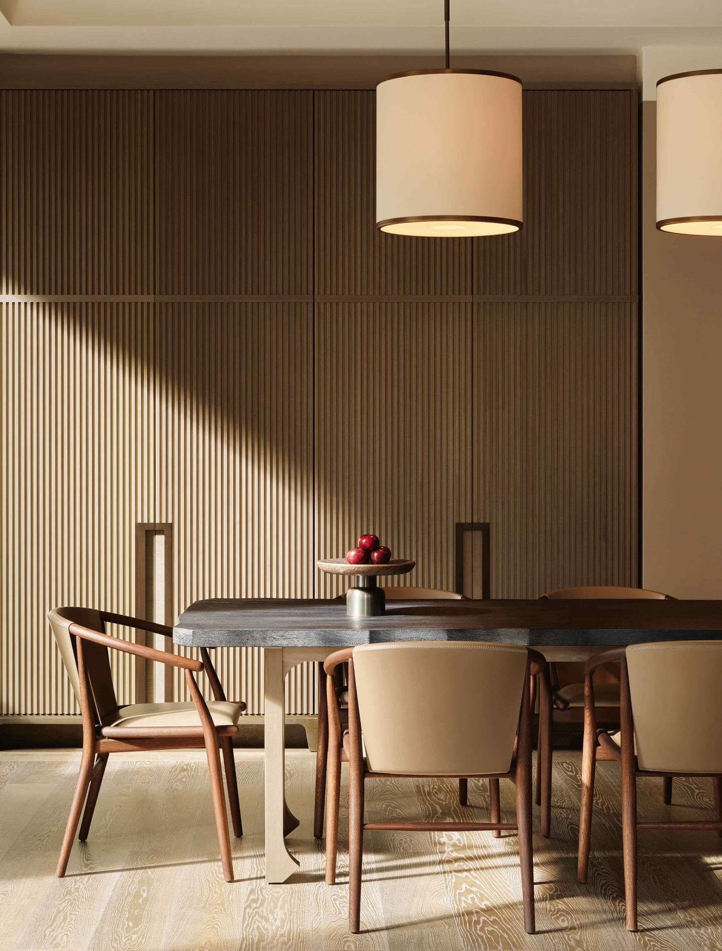 Aman New York, New York, United States — Mid-century dining room with walnut chairs, stone table, pendant lights, and vertical wood-slat wall paneling in warm neutral tones.