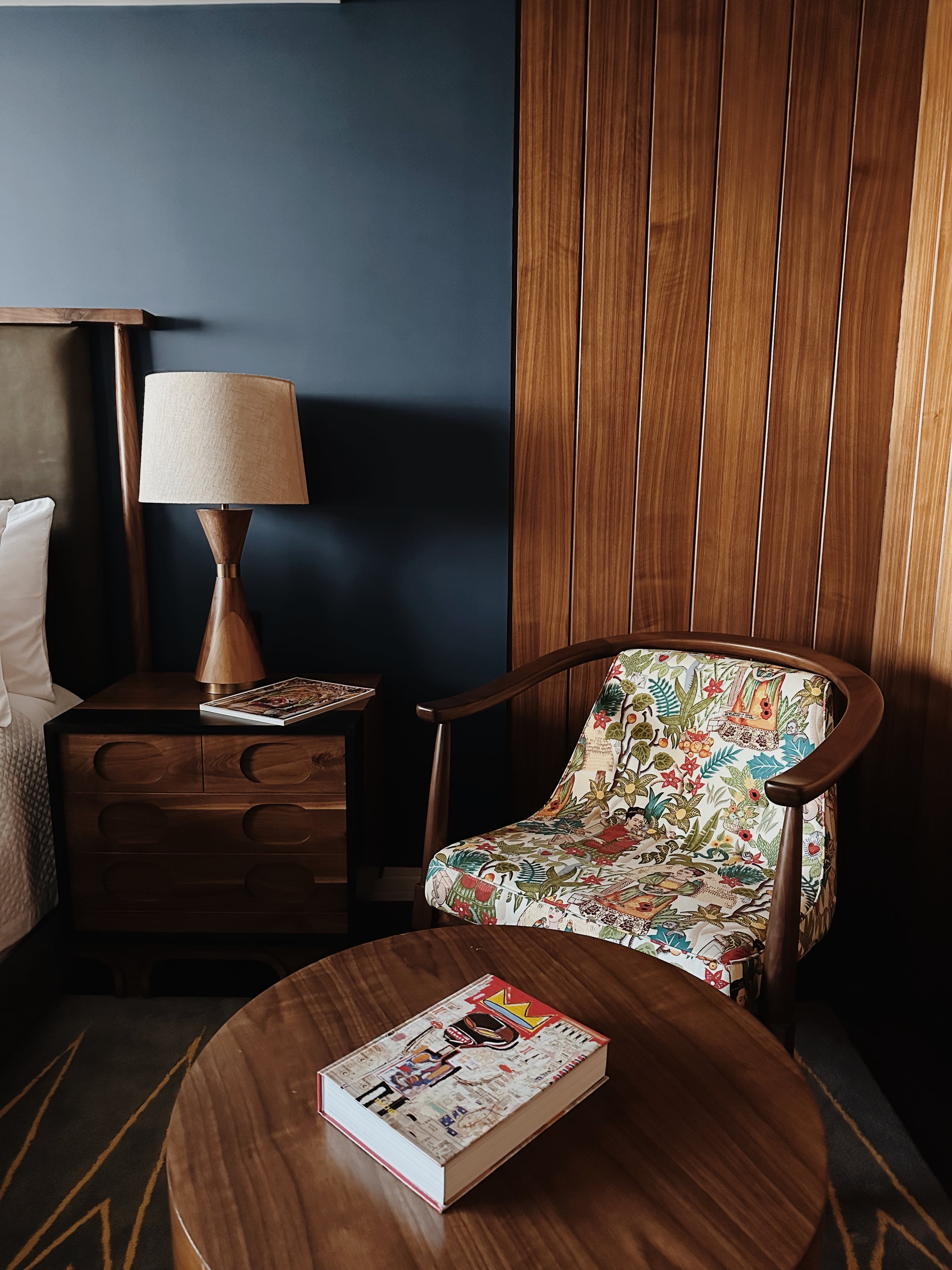 Campos Polanco, Mexico — Mid-century modern bedroom with walnut furniture, floral upholstered chair, cone table lamp, and slate blue accent wall.