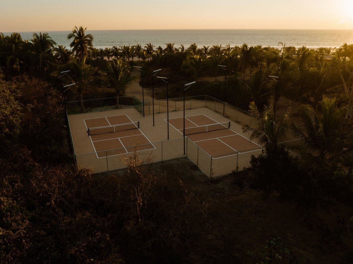Hotelito MUSA, Mexico — Clay tennis courts with palm trees and ocean horizon at golden hour, luxury coastal resort amenities.