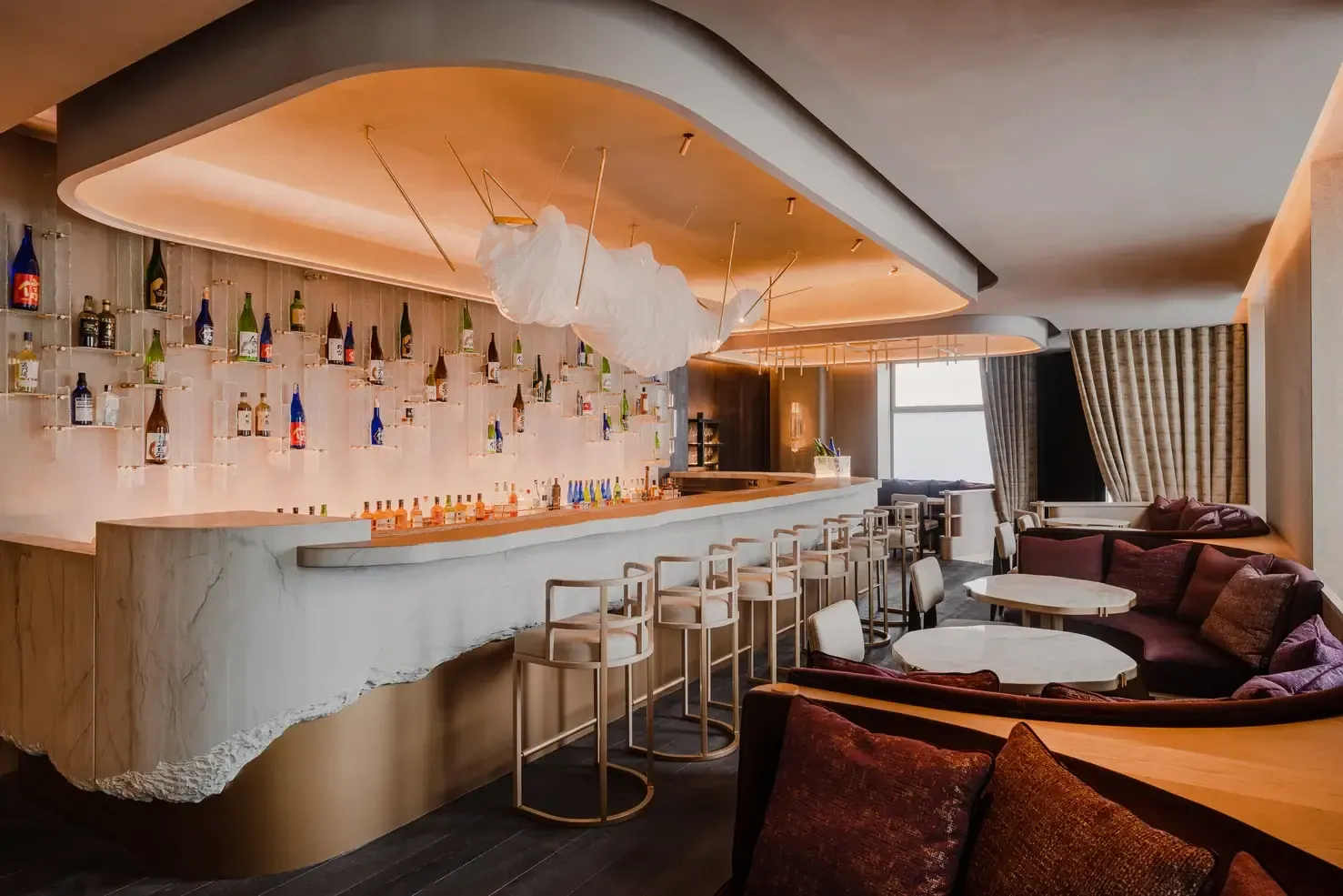 Sakebar by Nobu, Europe — minimalist bar with suspended bottles, curved orange ceiling, marble counter, brass stools, and burgundy lounge seating.