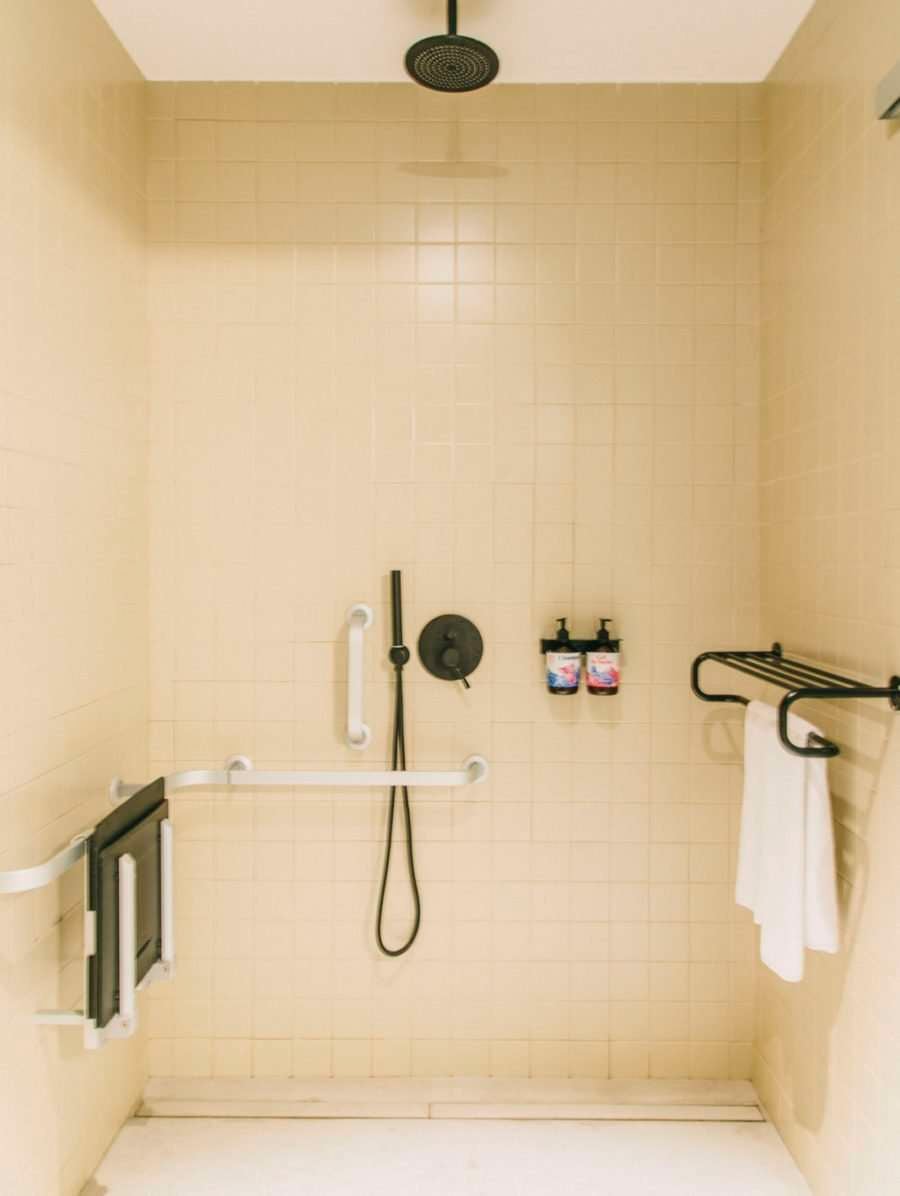 Casa Bonay, Europe — minimalist shower enclosure with cream subway tiles, black fixtures, rainfall showerhead, and monochromatic bath accessories.