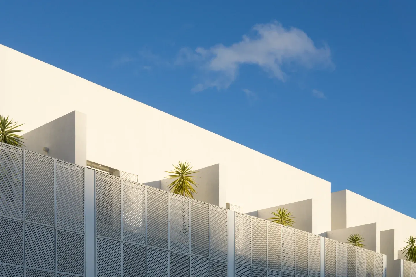 Casa Mãe, Europe — Minimalist white cubic architecture with perforated metal screening, cascading terraces, and sculptural palm plants against clear blue sky.