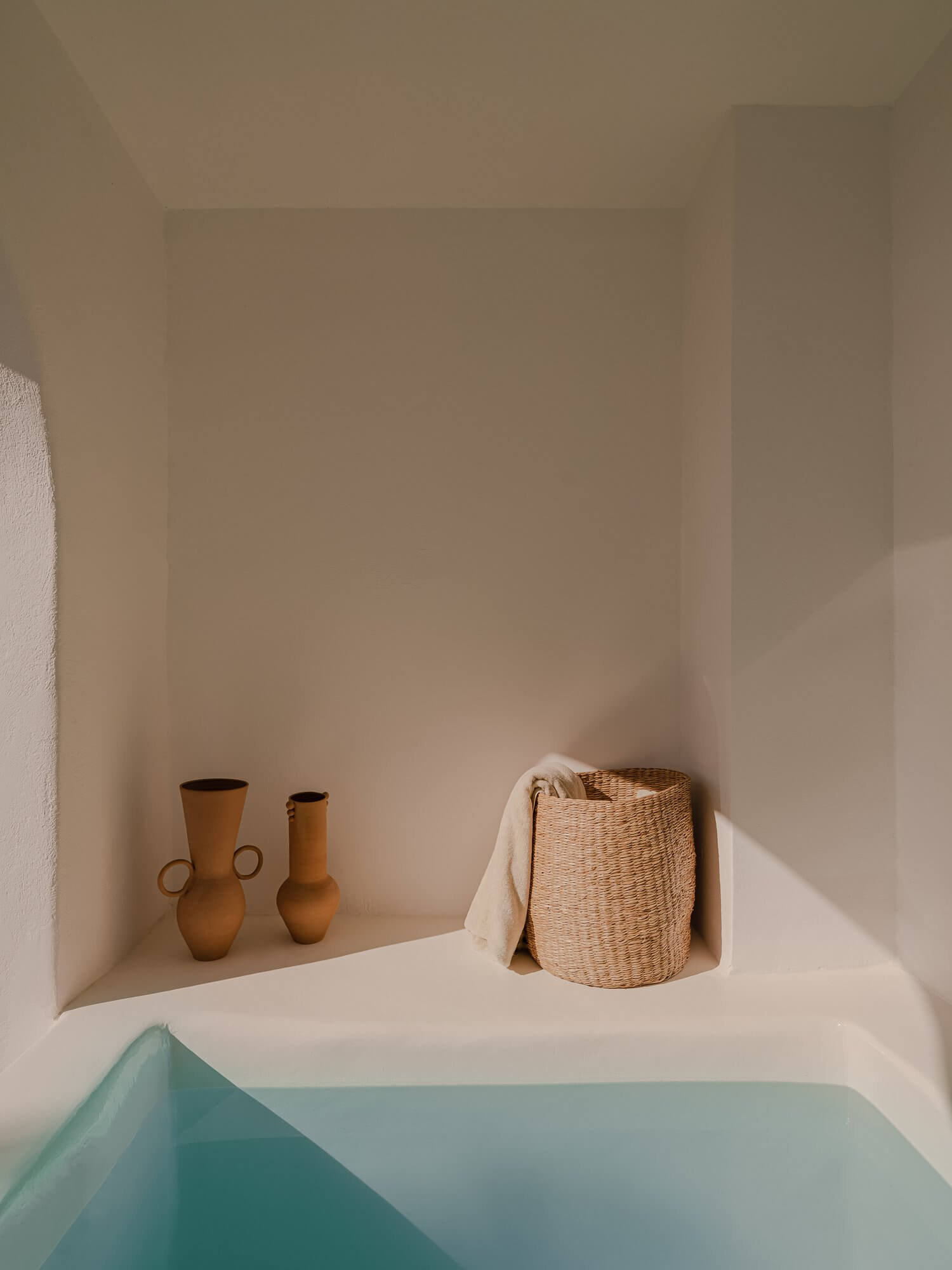 Nobu Santorini, Europe — Minimalist bathroom alcove with terracotta vessels, woven basket, and turquoise soaking tub in whitewashed architecture.