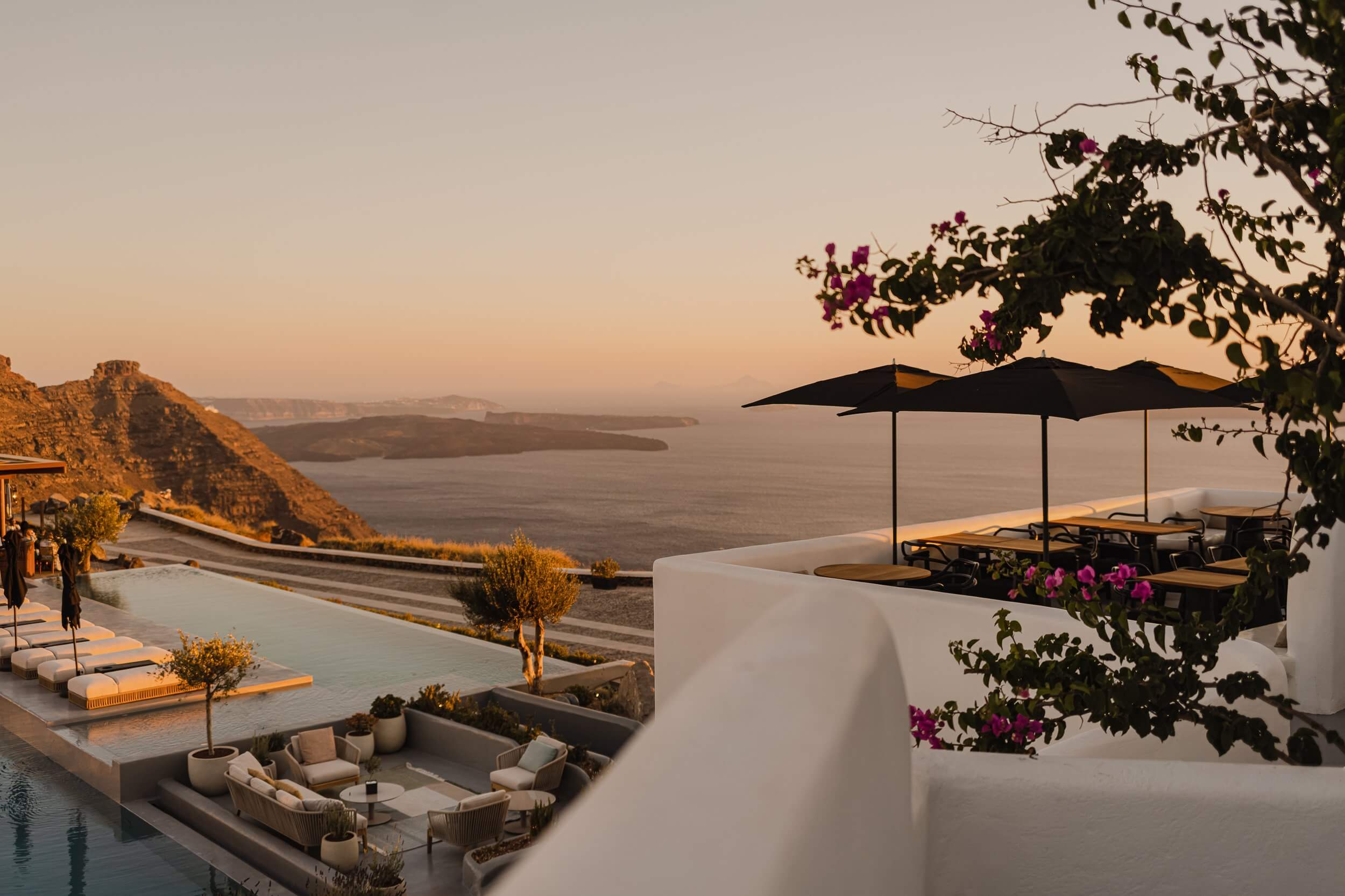 Nobu Santorini, Greece — Whitewashed terrace with magenta bougainvillea, black umbrellas, and sunken seating overlooking caldera at golden hour.