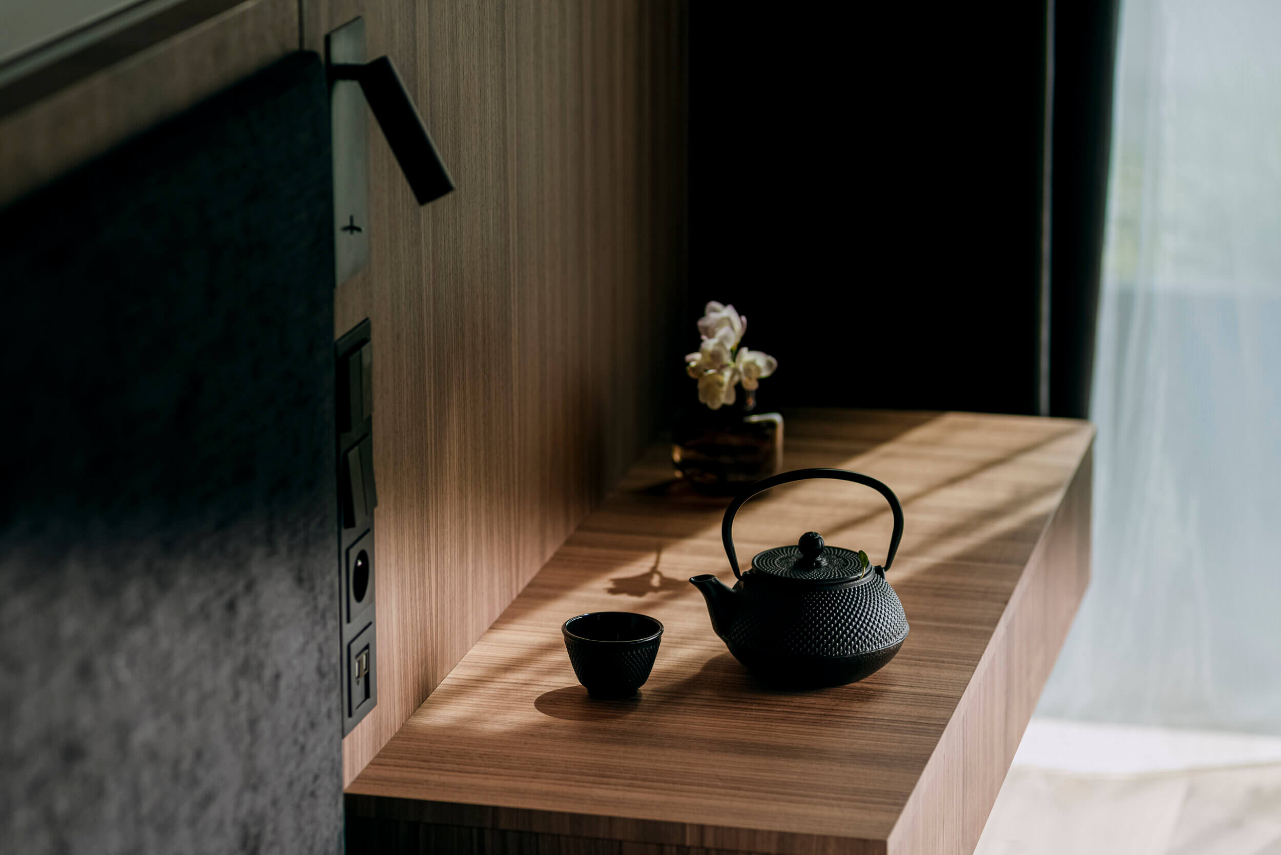 Nobu Warsaw, Poland — Black cast-iron teapot and cup on wooden shelf with sunlight and white iris flower, minimalist luxury hospitality interior design.