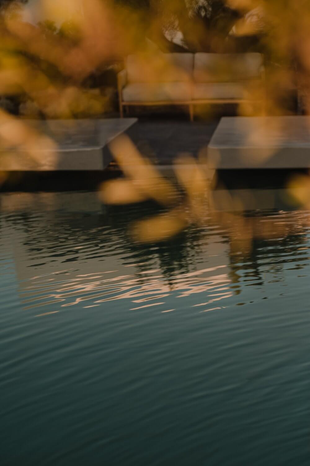 Nobu Spa, Europe — Warm golden light reflects on still spa water as barefoot guests wade through shallow pool with wooden deck and lounge seating.