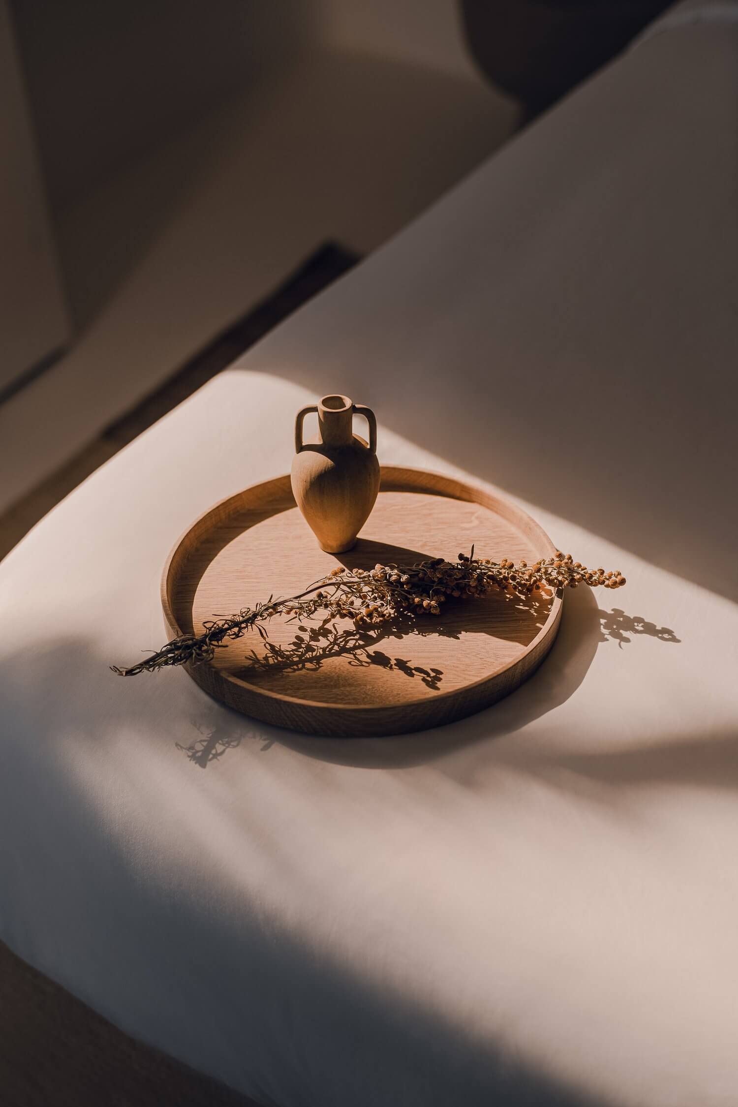 Nobu Santorini, Europe — Wooden tray with terracotta amphora vessel and dried botanicals, sunlit minimalist still life arrangement.
