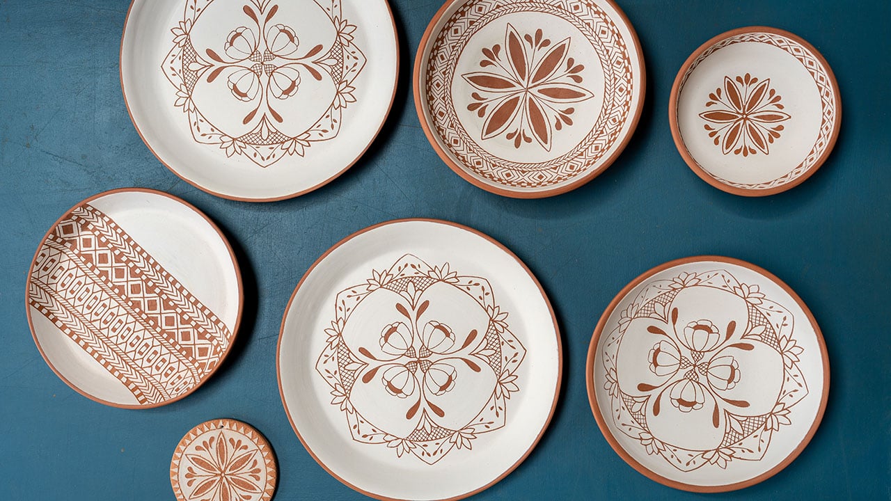 Pottery Workshop — Handcrafted terracotta plates with rust-brown geometric and floral patterns arranged on deep teal surface, showcasing artisanal pottery design.