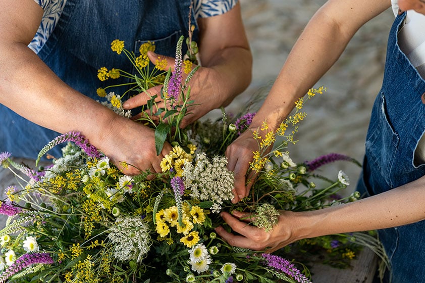 Flower Workshop, Europe — Hands arranging wildflowers in yellow, white, and purple blooms with green stems, intimate craft activity near luxury hotel.