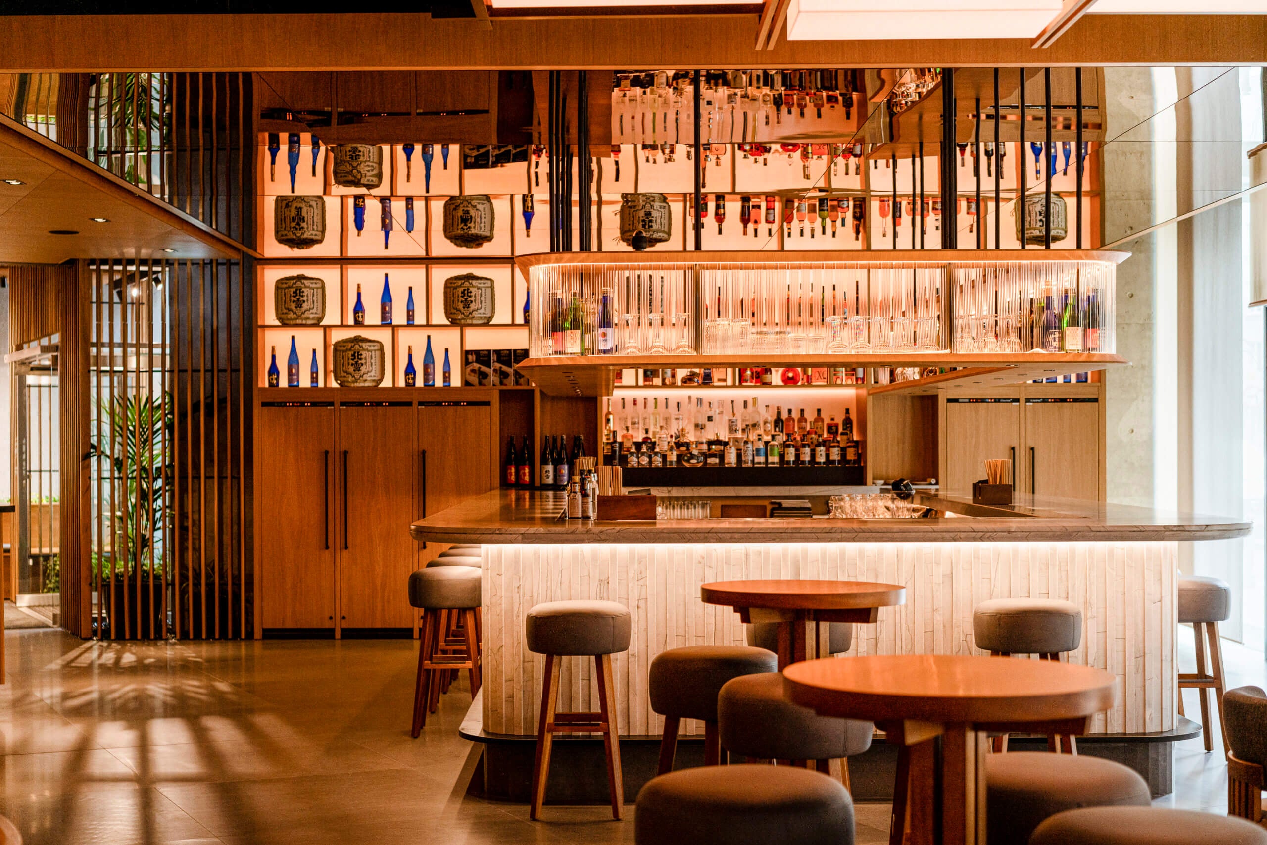Nobu Bar, Europe — Warm wood interior with backlit shelving, mid-century stools, geometric tile work, and elegant bottle displays above polished counter.