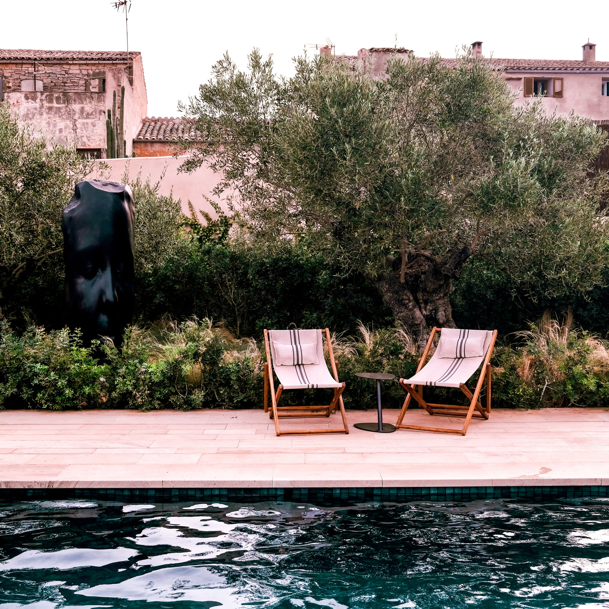 Can Ferrereta, Balearic Islands, Spain — Two striped loungers on terracotta poolside deck facing olive grove and pink-rendered stone villa architecture.