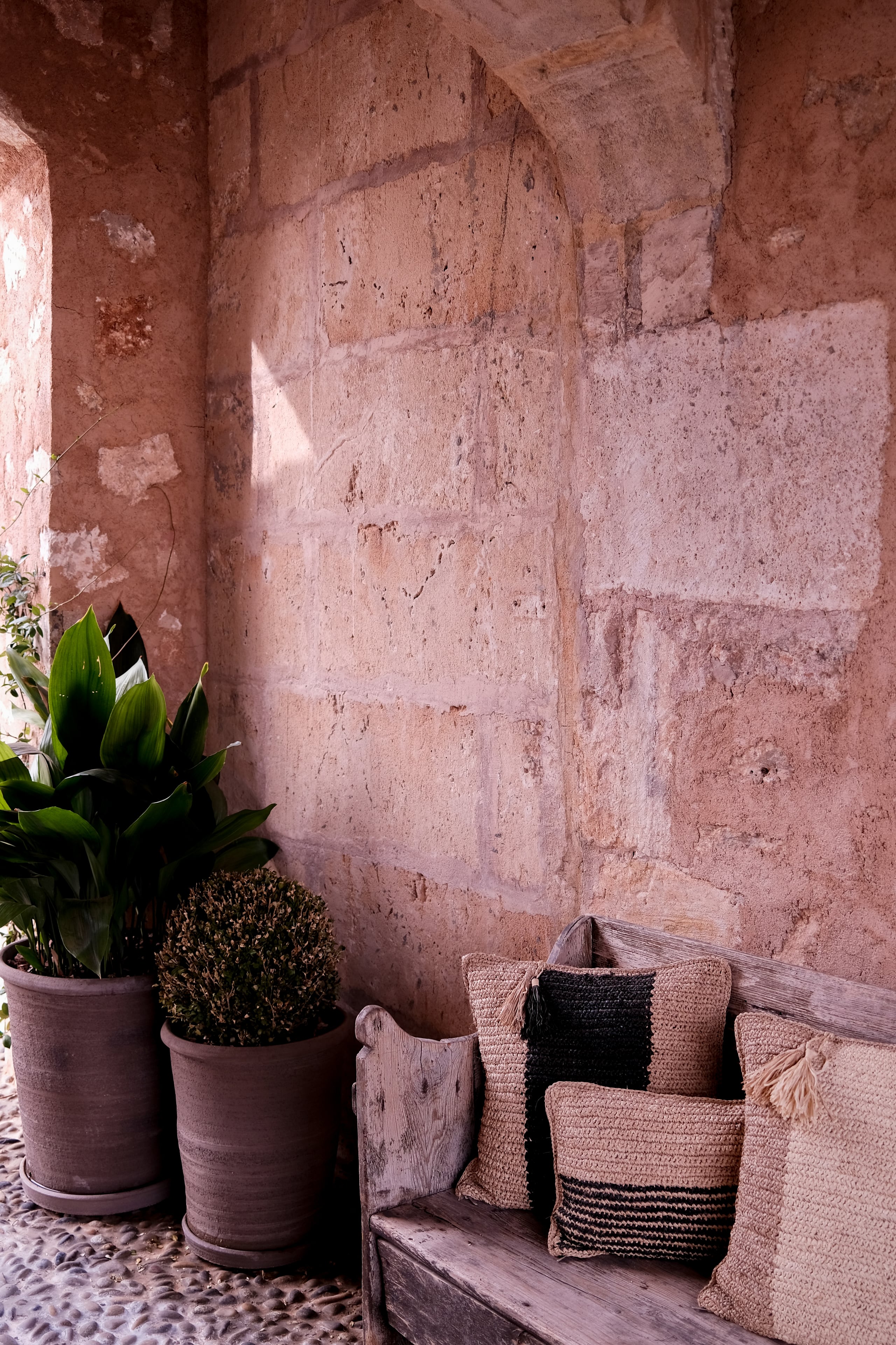 Can Ferrereta, Balearic Islands, Spain — Terracotta courtyard with potted plants, woven baskets, and weathered wooden bench against textured stone wall in afternoon light.