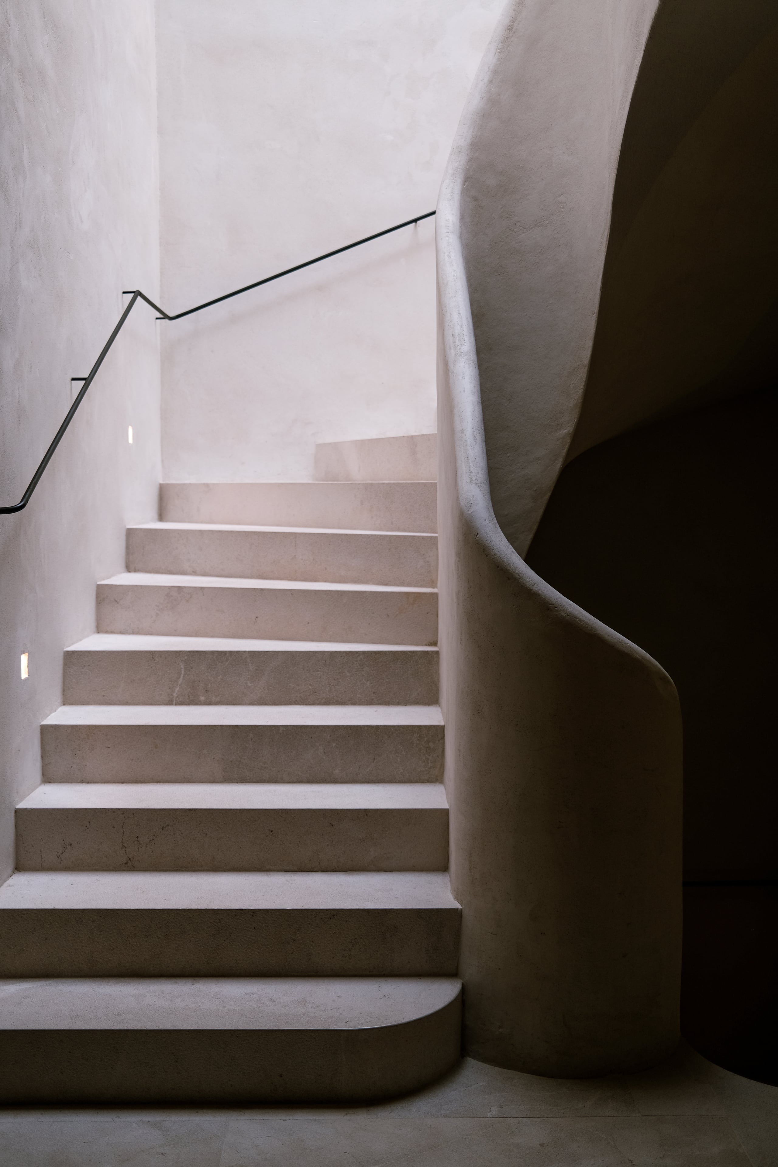 Can Ferrereta, Balearic Islands, Spain — Minimalist concrete staircase with curved sculptural wall and metal handrail, modernist architecture in neutral tones.