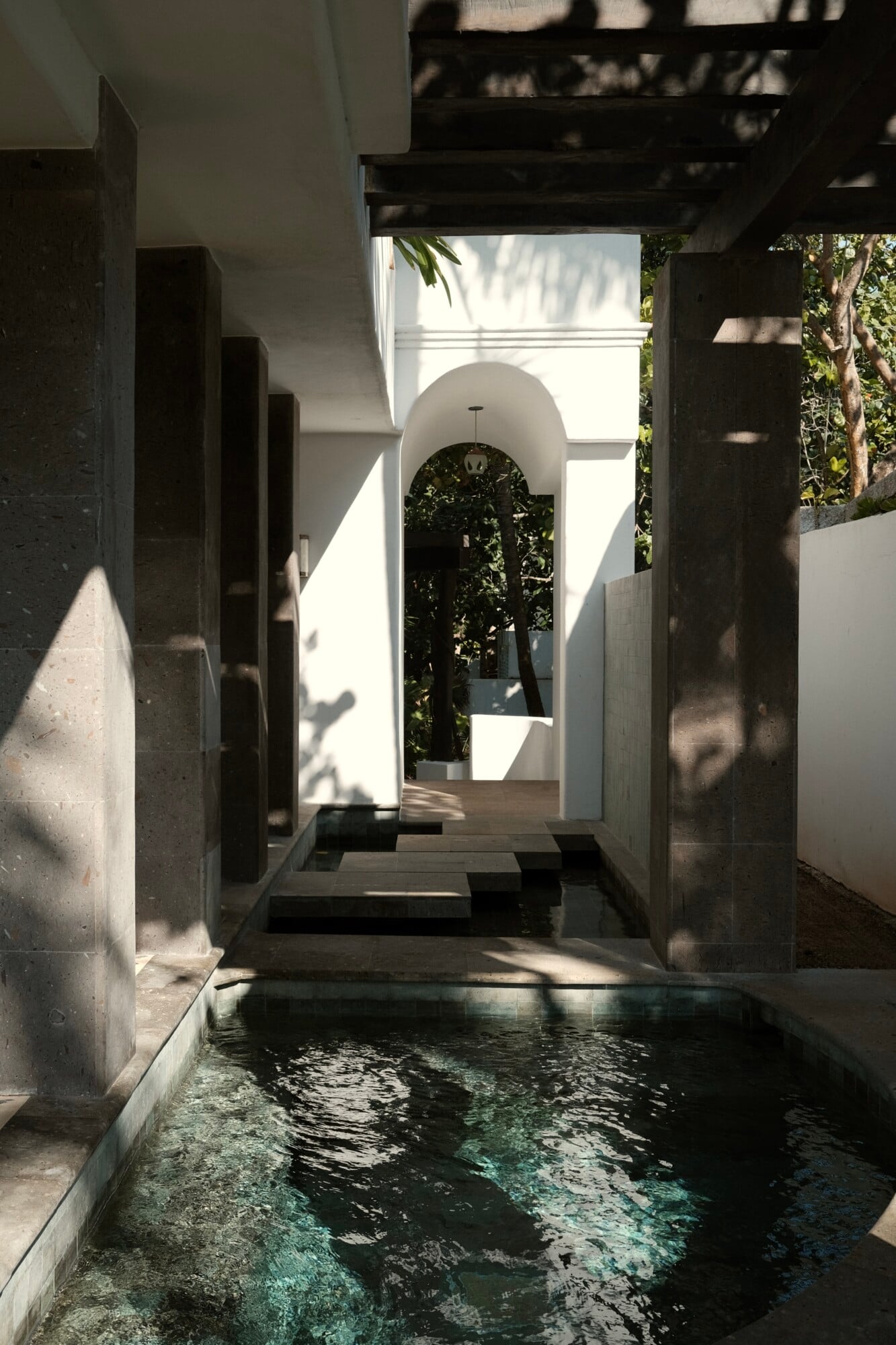 Maroma, A Belmond Hotel, Mexico — Narrow water passage with dark stone walls, arched white corridor, dappled shadows, tropical greenery beyond.