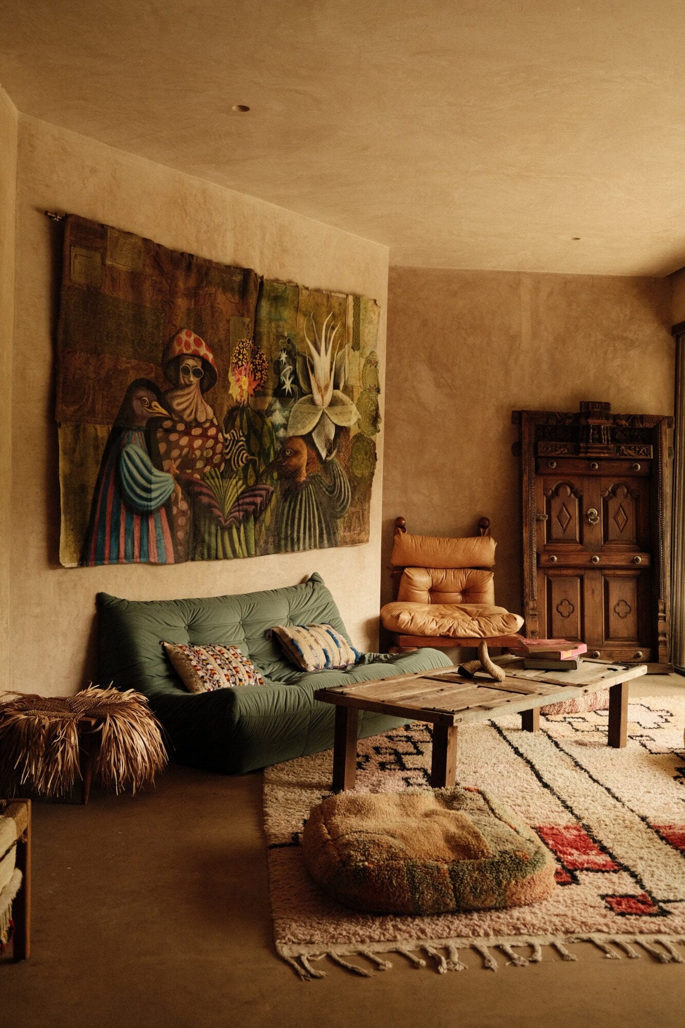 Casa Lumeria, Mexico — Ochre-walled living room with green linen sofa, carved wooden furniture, textile art, woven rugs, and natural light creating warm, earthy bohemian atmosphere.