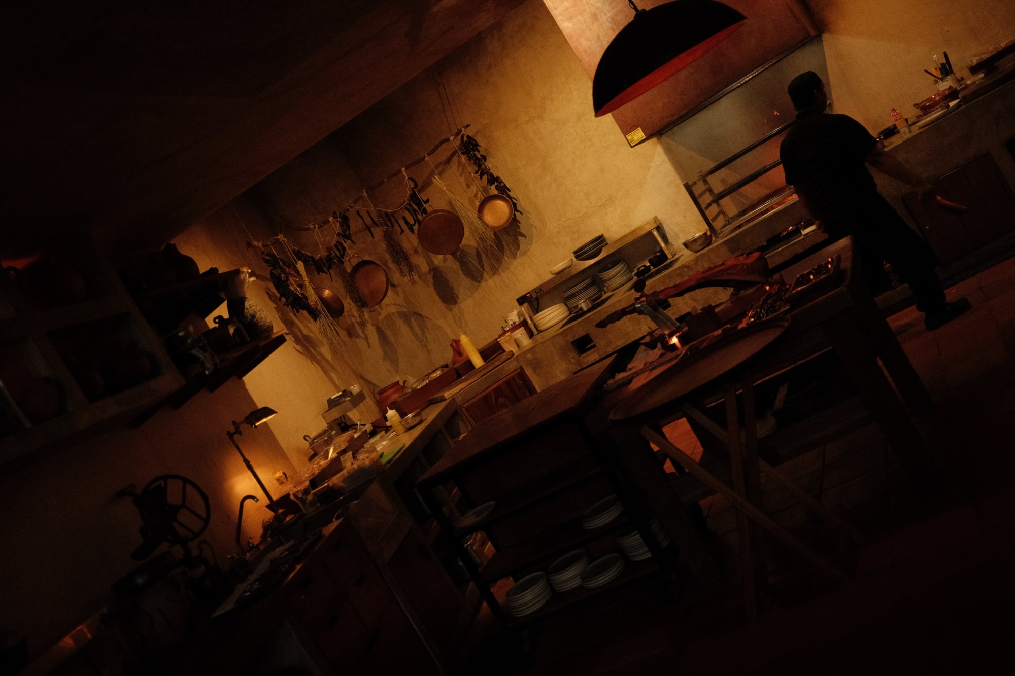 Zapote Bar, Mexico — Warm-lit rustic interior with clay vessels hung on ochre walls, wooden tables, and silhouetted figures in intimate hospitality setting.