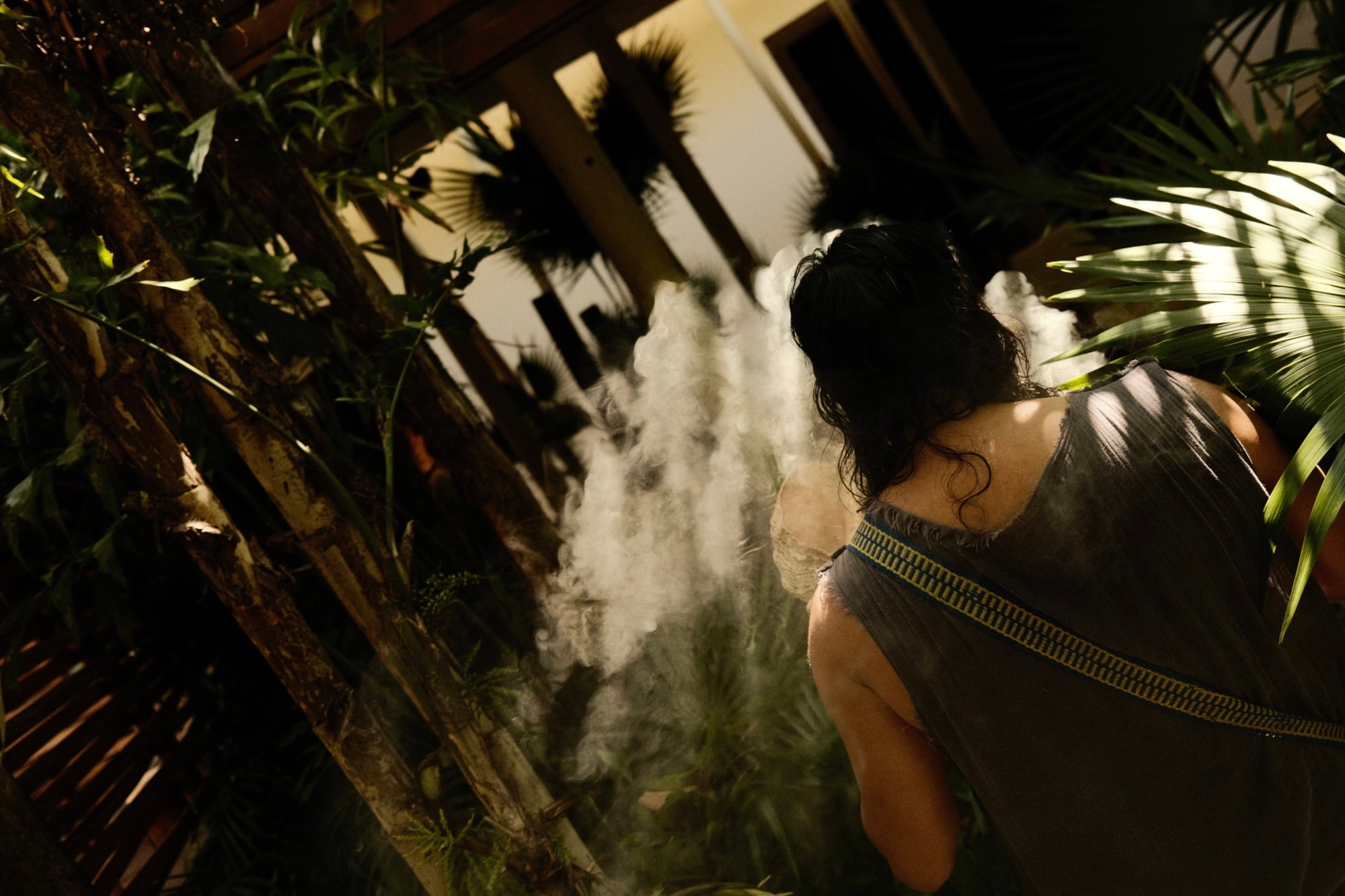 Sense, A Rosewood Spa, Mexico — woman in spa treatment room surrounded by tropical plants, dramatic light and mist creating ethereal atmosphere in luxury wellness sanctuary