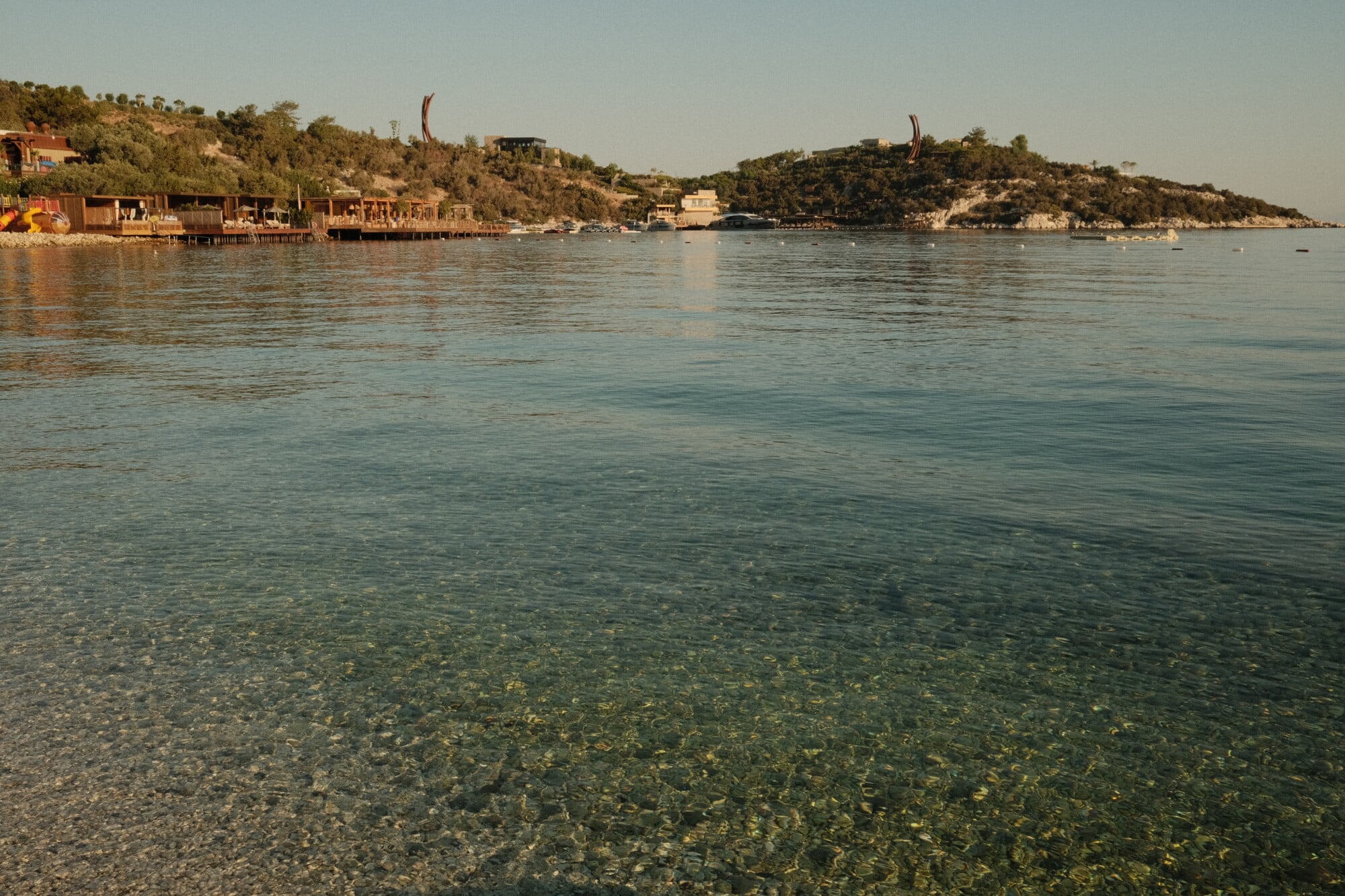 Mandarin Oriental Bodrum, Turkey — Turquoise Aegean waters with wooden waterfront villas nestled against pine-covered hillside under clear sky.