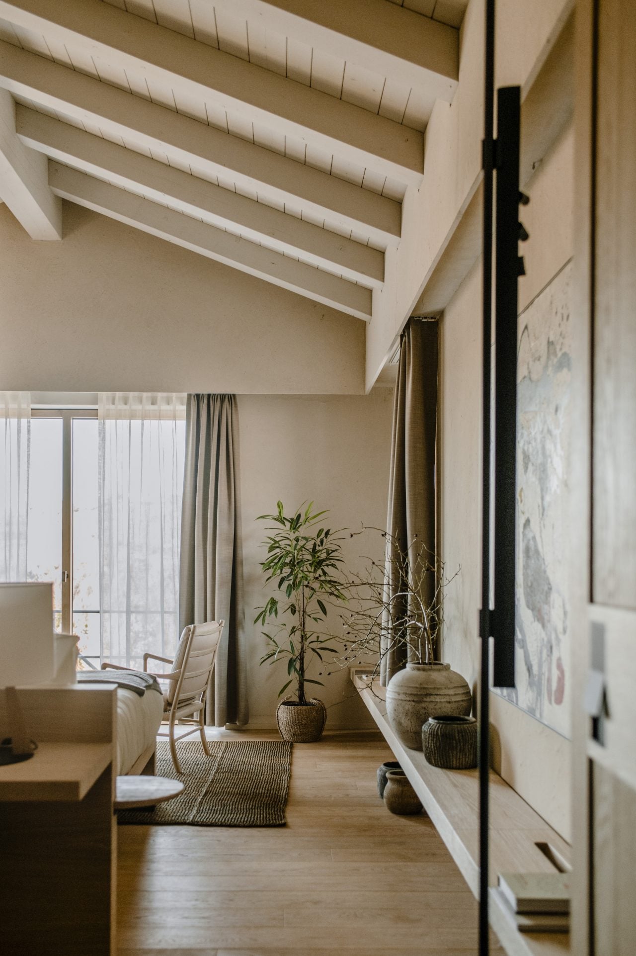 Casa di Langa, Europe — Minimalist bedroom with coffered ceiling, floor-to-ceiling windows, potted plants, and natural linen furnishings in warm neutral tones.