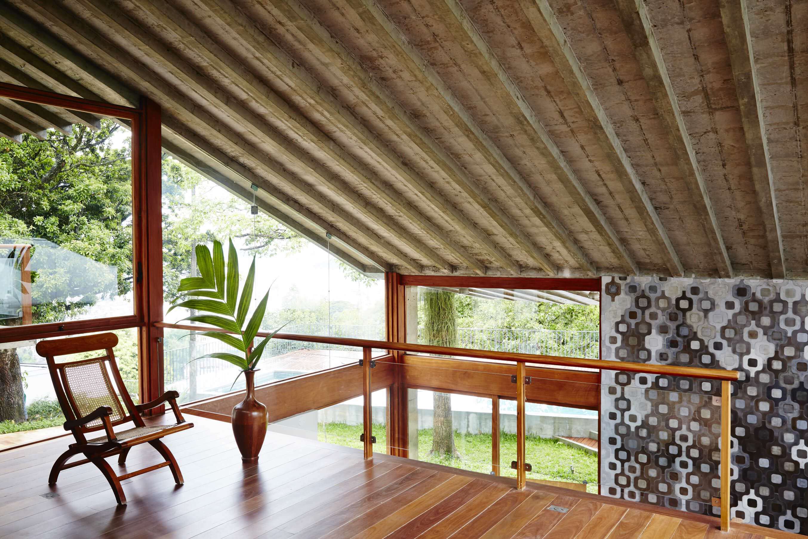 Chez Georges, South America — Modern pavilion with exposed wooden ceiling beams, floor-to-glass walls, teak furnishings, and geometric concrete screening overlooking landscaped grounds.