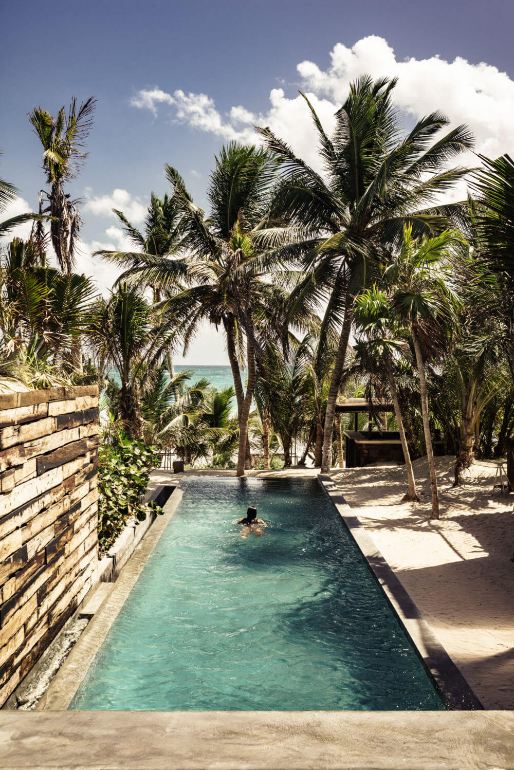 Be Tulum, Mexico — Narrow infinity pool flanked by palm trees with ocean view, natural light and turquoise water creating serene coastal luxury aesthetic.