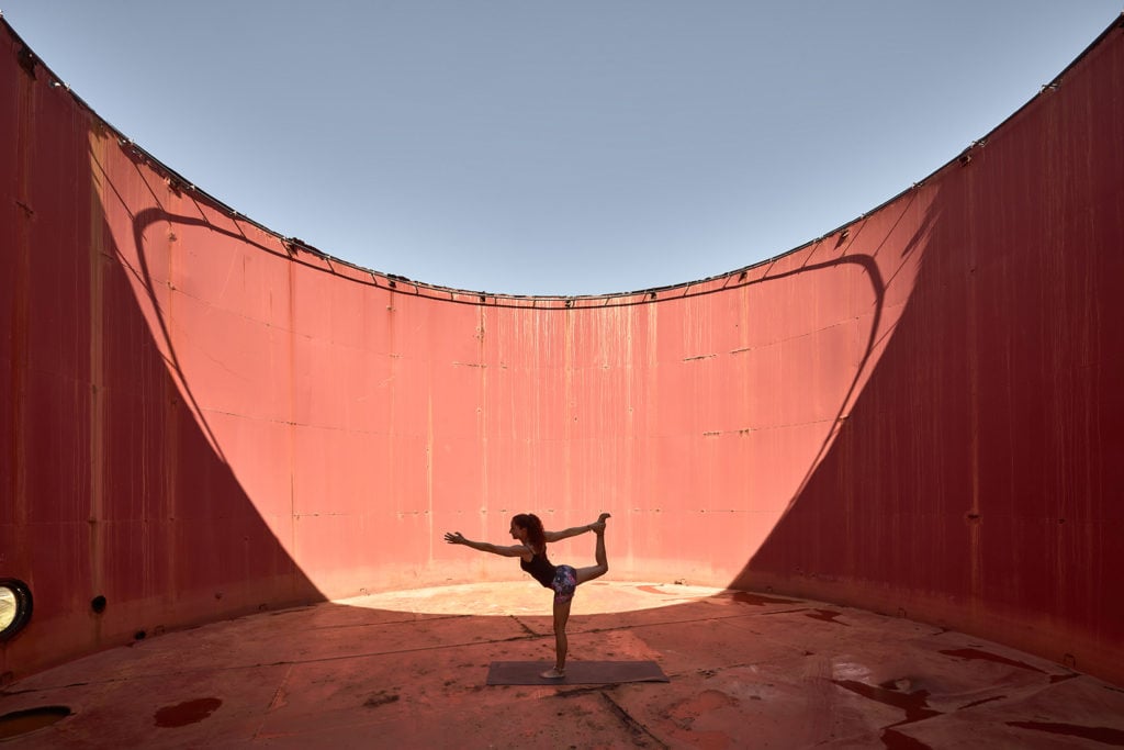 Dexamenes Seaside Hotel, Europe — Woman in yoga pose inside curved red shipping container with natural light, industrial architecture.