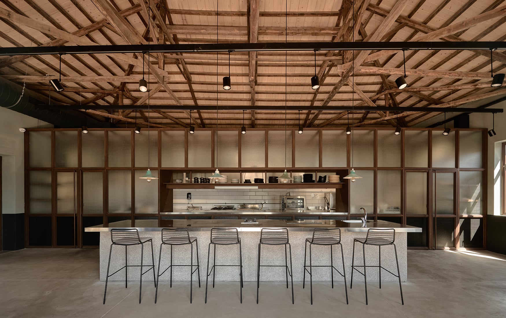 Ex-Engine Room Restaurant, Europe — Industrial kitchen with exposed wooden ceiling beams, frosted glass cabinetry, concrete island counter, and minimalist bar seating.