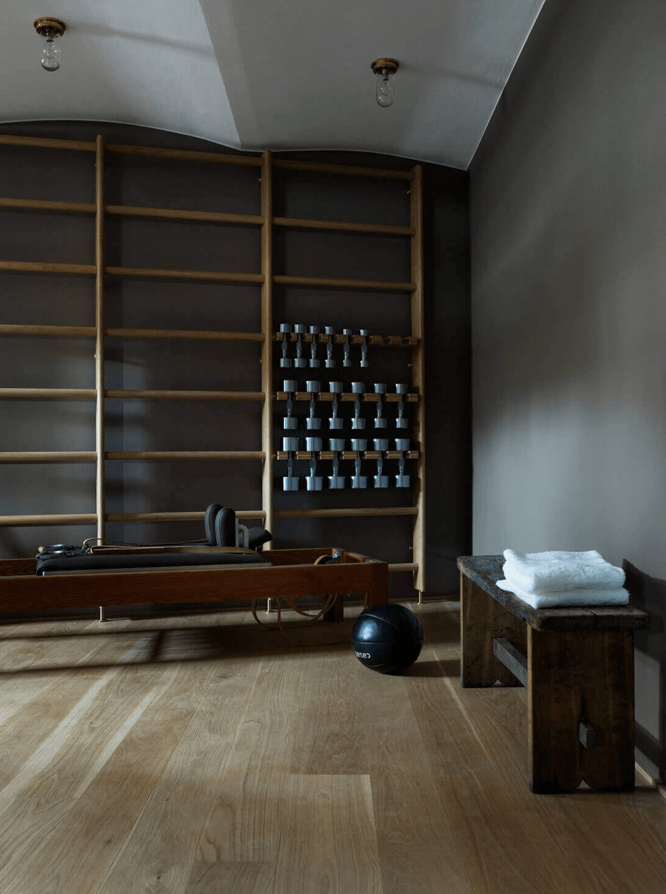 Ett Hem, Europe — Minimalist fitness studio with wooden shelving, dumbbell rack, exercise equipment, and light oak flooring beneath white ceiling.