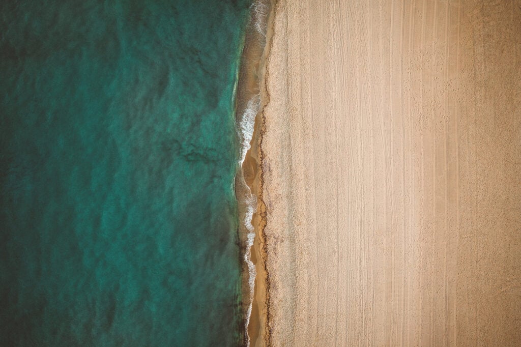 Epi 1959, Europe — Aerial view of pristine sandy beach meeting turquoise waters with white wave breaking along shoreline, minimalist coastal landscape.