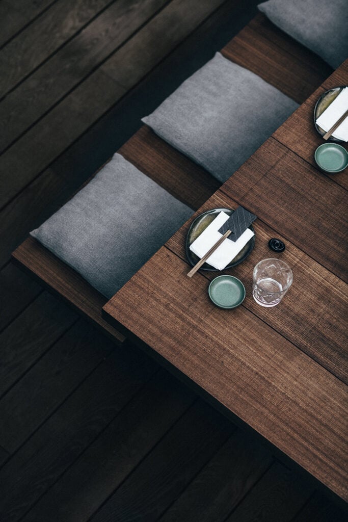 Epi 1959, Europe — Minimalist dining setup with gray upholstered chairs, walnut table, place settings with sage ceramic bowls and glassware on dark wooden flooring.