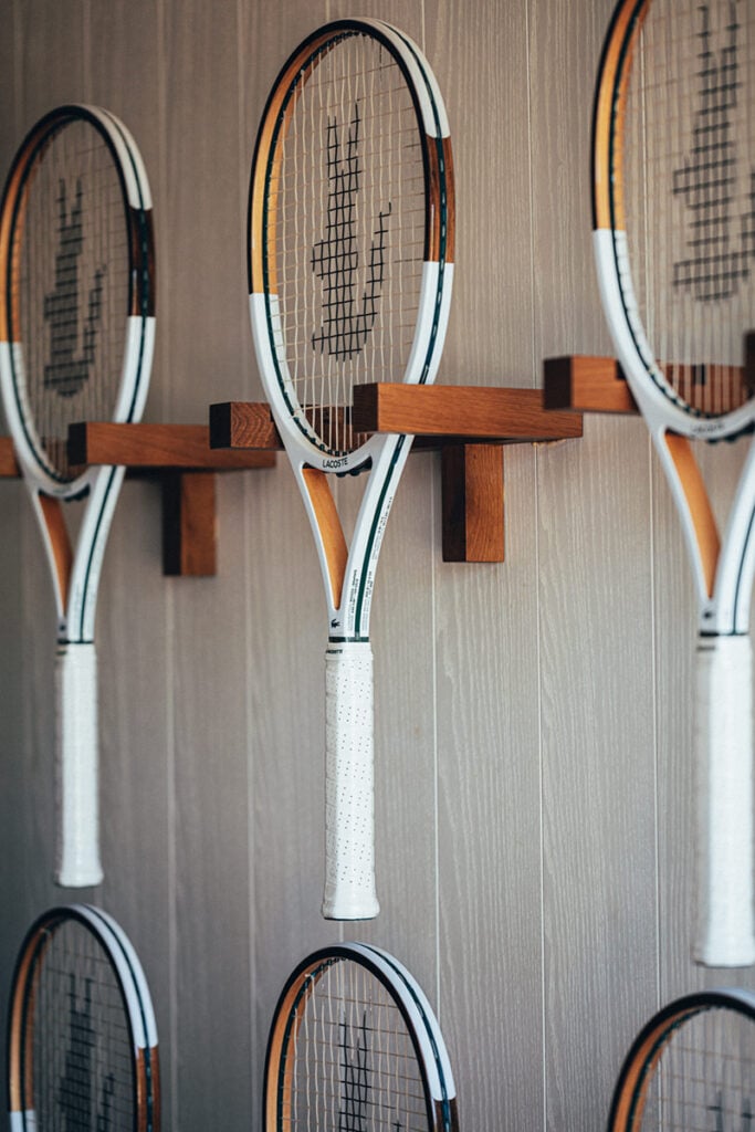 Epi 1959, Europe — Tennis rackets with orange and white frames mounted on wooden wall rack, minimalist sports display.