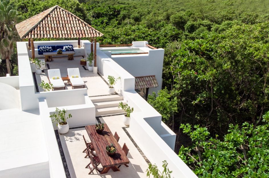 Hotel Esencia, Mexico — Modernist white terraces overlooking jungle canopy with teak furniture, loungers, and ceramic planters in dappled sunlight.