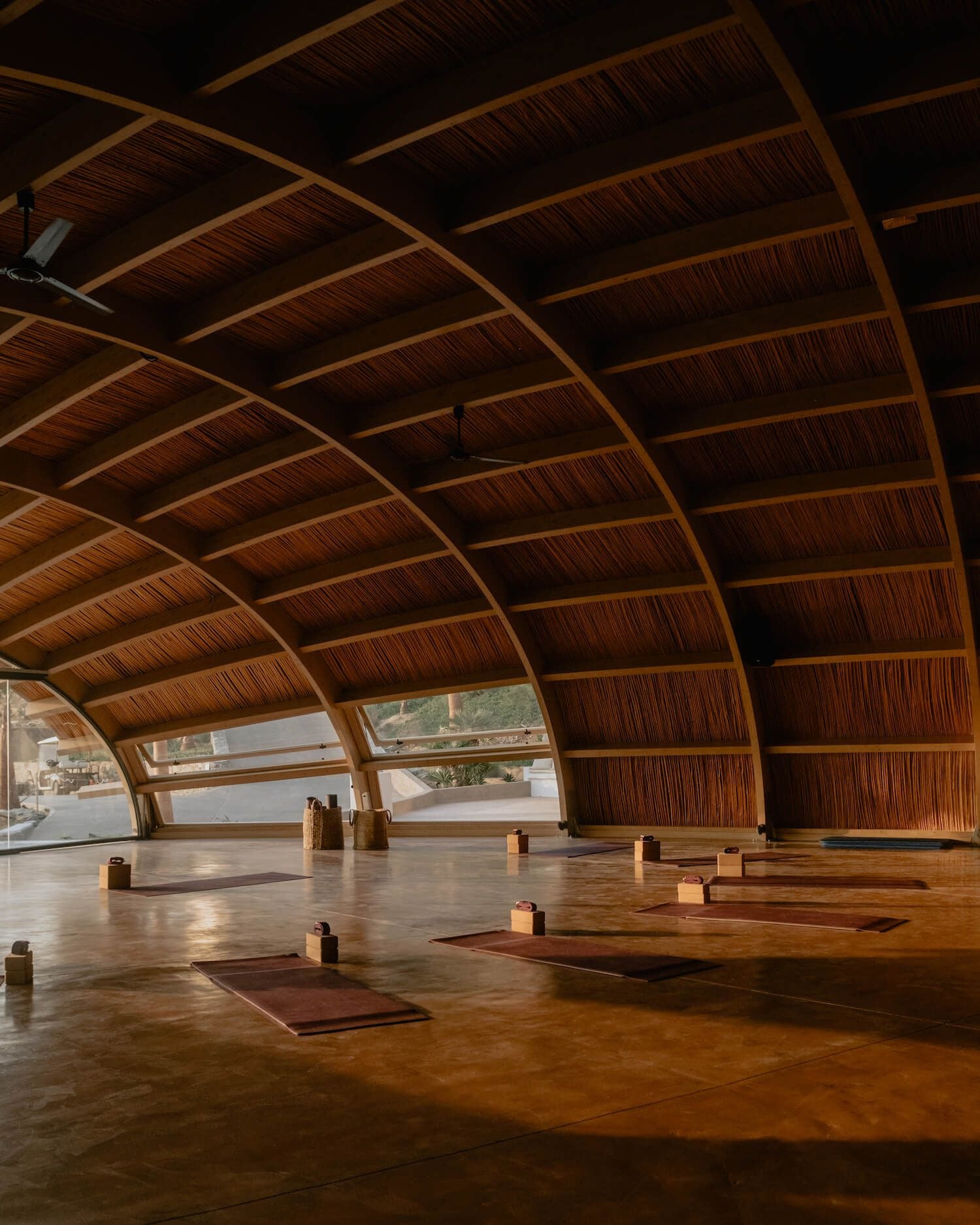 ACRO Suites, Europe — Curved wooden ceiling with geometric beams and floor yoga mats in minimalist wellness studio with panoramic windows.