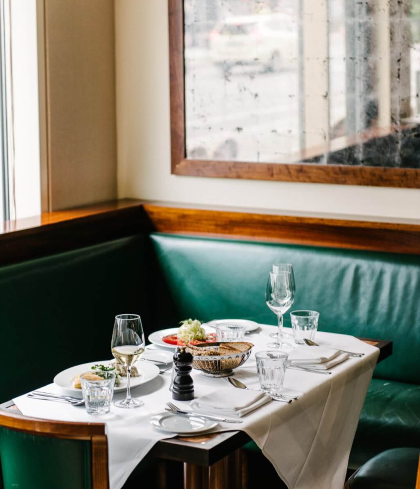 Einstein Unter den Linden, Berlin, Germany — Elegant dining booth with green leather banquette, white tablecloth, wood paneling, and city views through tall windows.