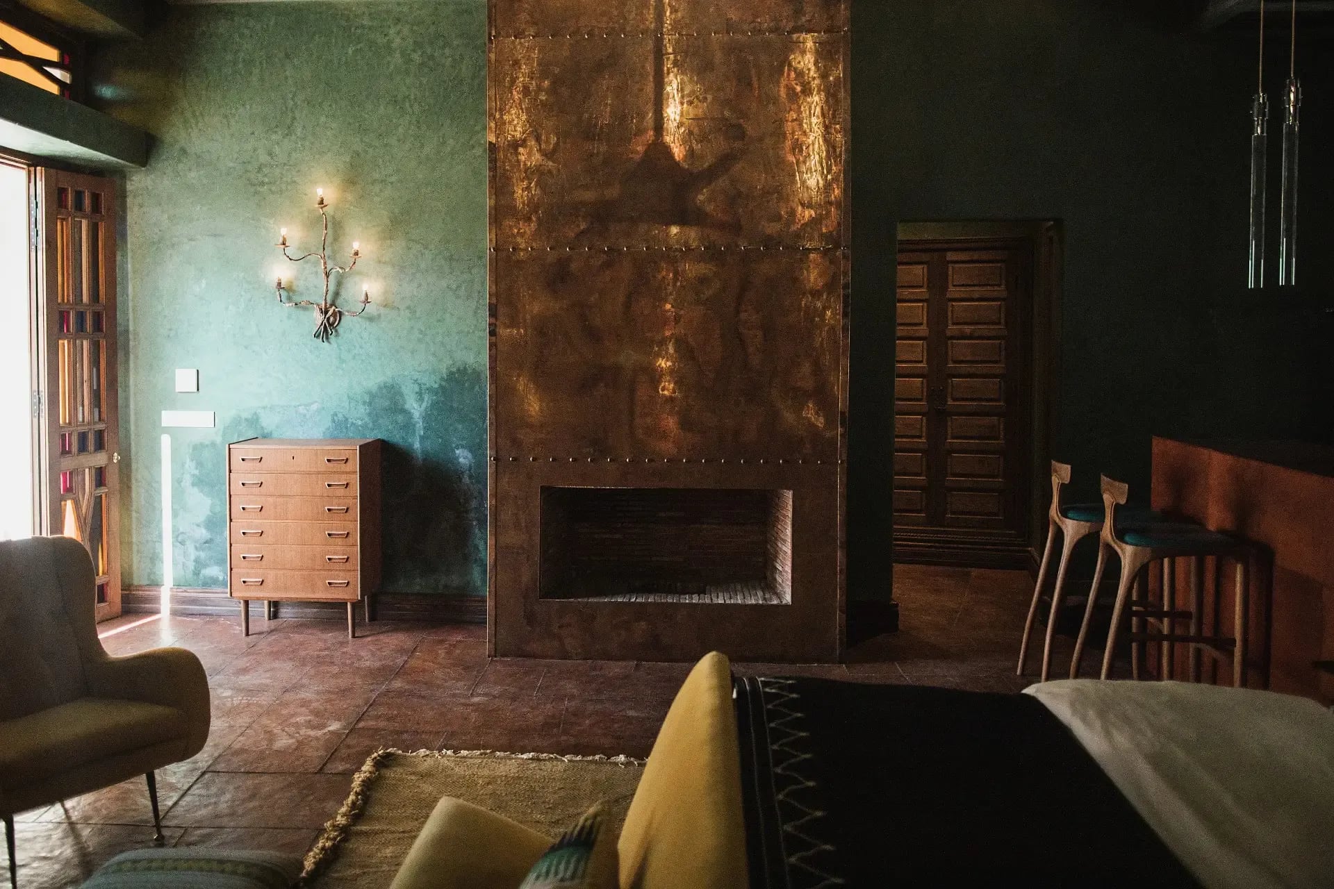 El Fenn, Africa — Ochre oxidized-metal fireplace surround, turquoise plaster walls, mid-century furniture, and natural light in minimalist luxury interior.