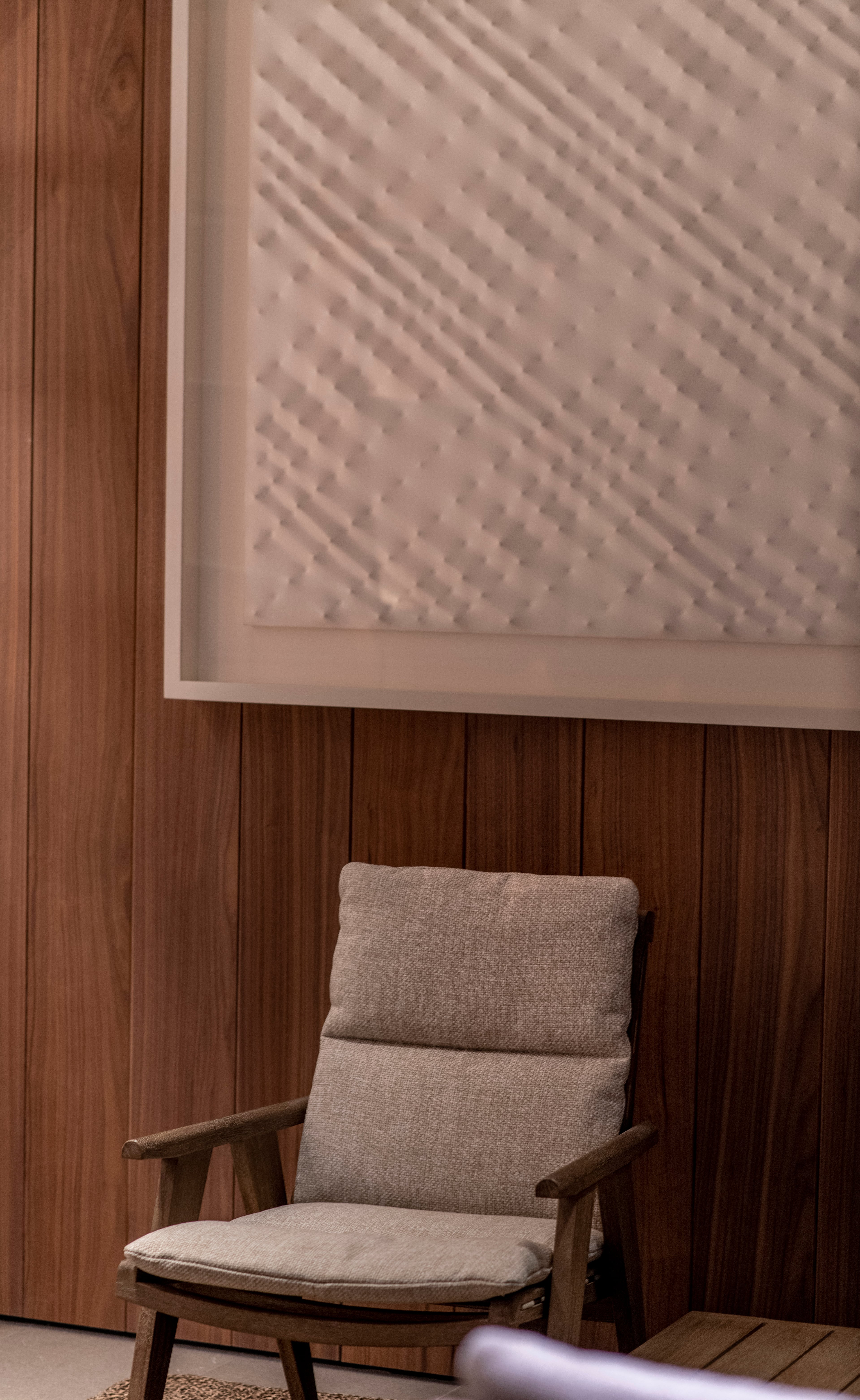 Casa di Langa, Europe — Mid-century wooden armchair with linen cushions beside paneled walnut wall and geometric textured ceiling detail.