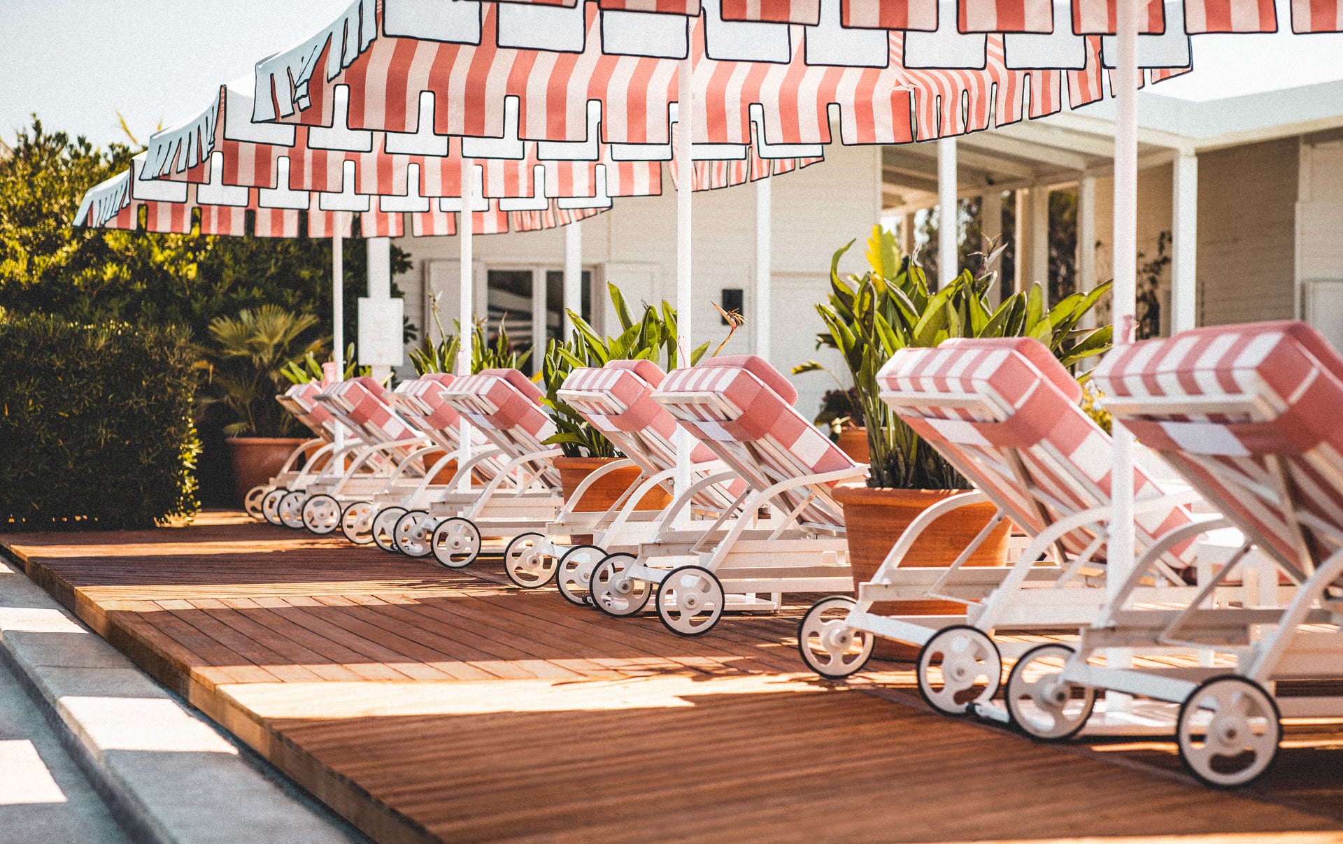 Epi 1959, Europe — Red-and-white striped loungers and umbrellas on wooden deck with potted plants and modernist architecture in afternoon light.