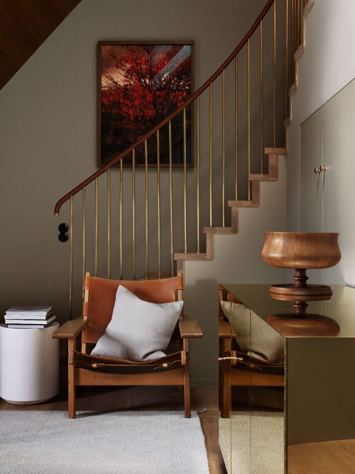 Ett Hem, Europe — Minimalist stairwell with wooden mid-century chairs, brass railings, and red landscape artwork overlooking gallery space.