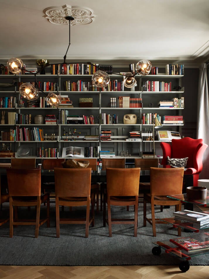 Ett Hem, Europe — Charcoal library with floating brass pendant lights, cognac leather chairs, red velvet seating, and ornamental ceiling rose detail.