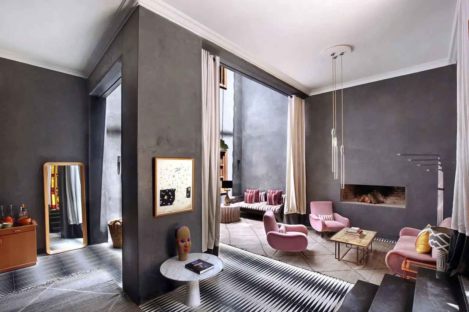 El Fenn, Africa — Charcoal walls and white ceiling frame pink velvet chairs, marble fireplace, pendant lights, and floor-to-ceiling windows in luxury hotel suite.