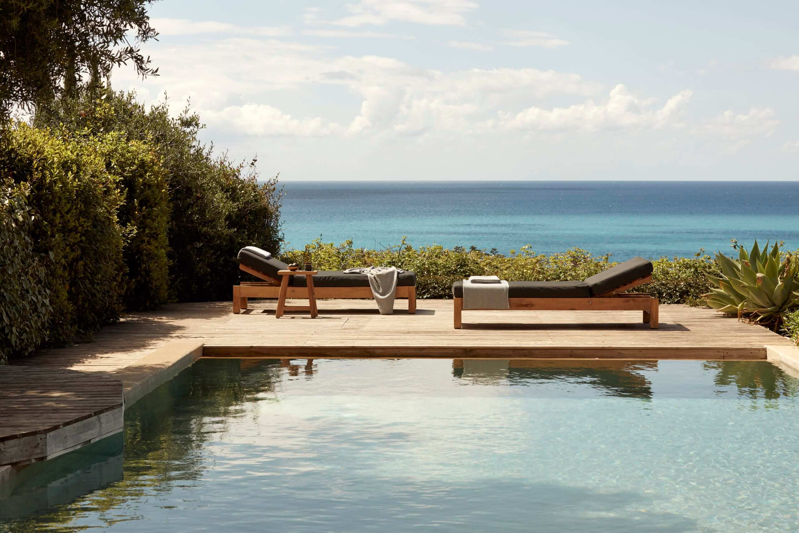 F Zeen Retreat, Europe — Wooden lounge chairs on terrace overlooking infinity pool and Mediterranean Sea, minimalist coastal luxury design.