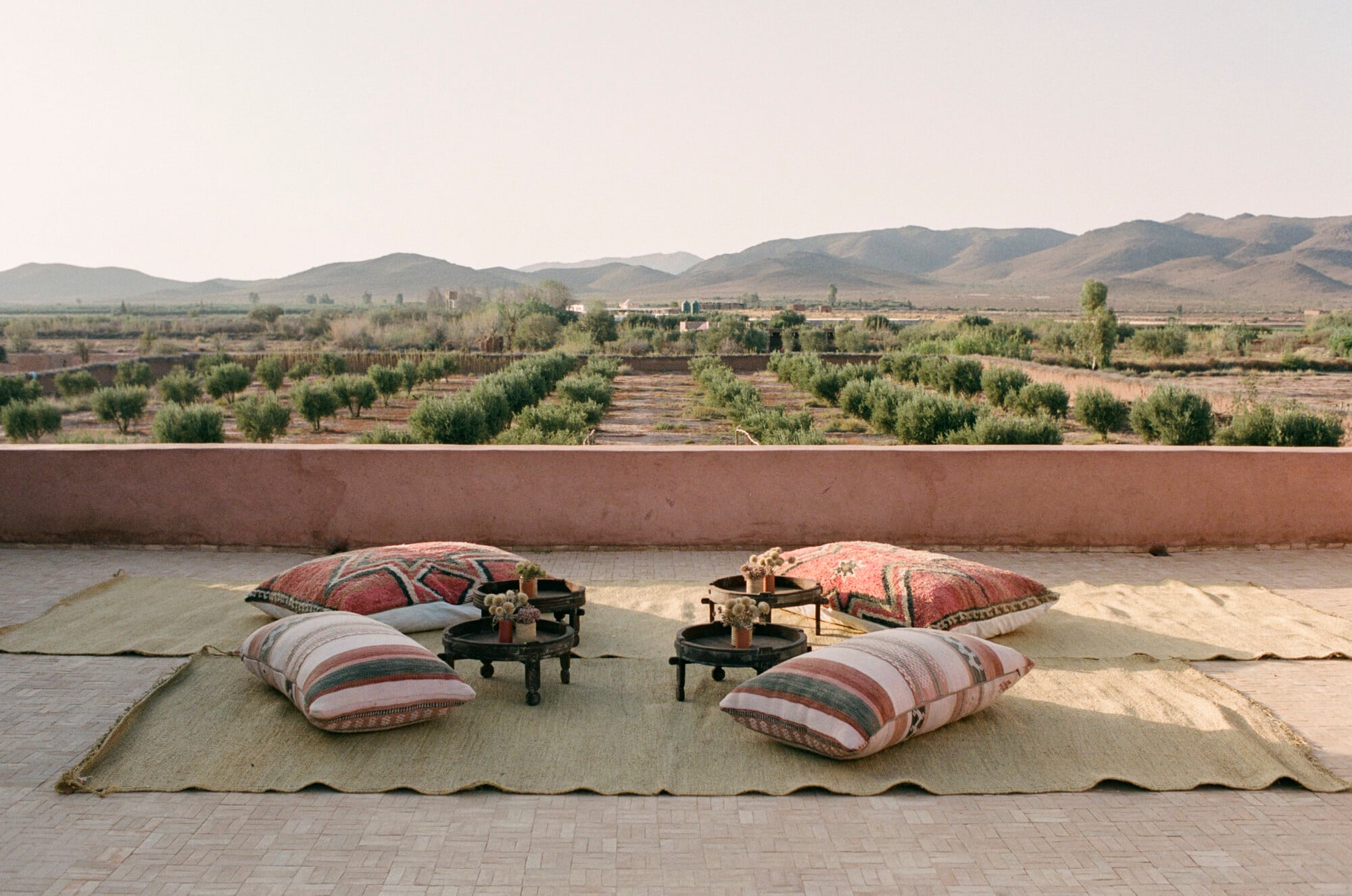 Farasha Farmhouse, Africa — Rooftop seating with striped cushions and low tables overlooking olive groves and desert mountains at dusk.
