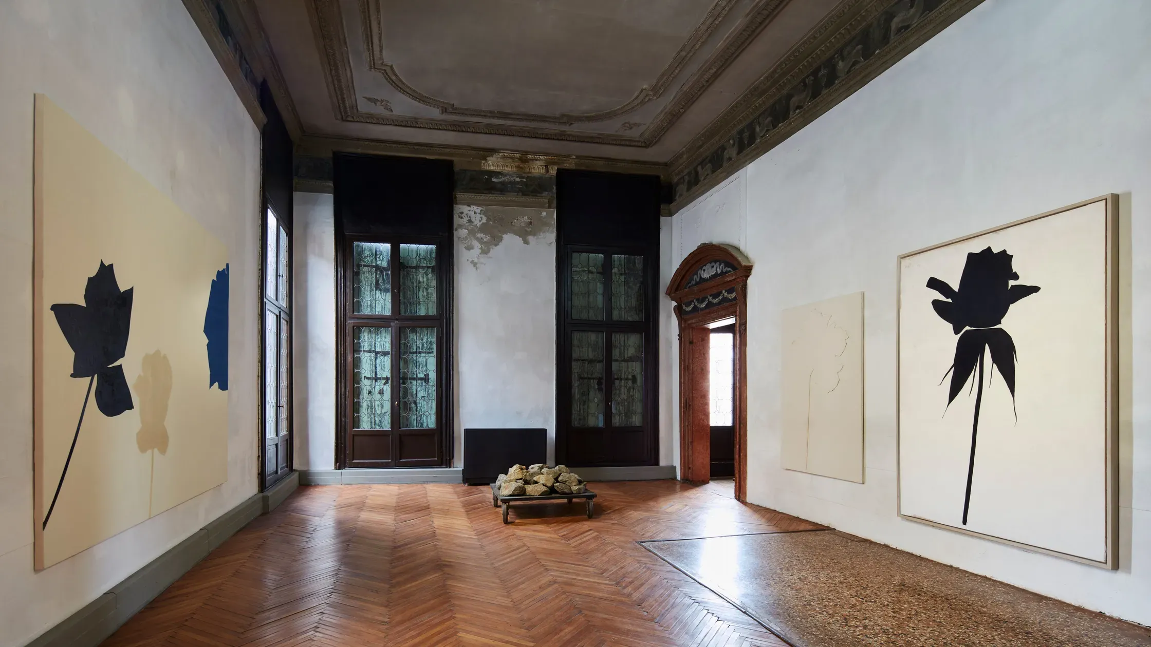 Fondazione Prada Venezia, Venice, Italy — Minimalist gallery with black silhouette artworks on cream walls, herringbone wood flooring, ornate ceiling, and natural light from tall windows.