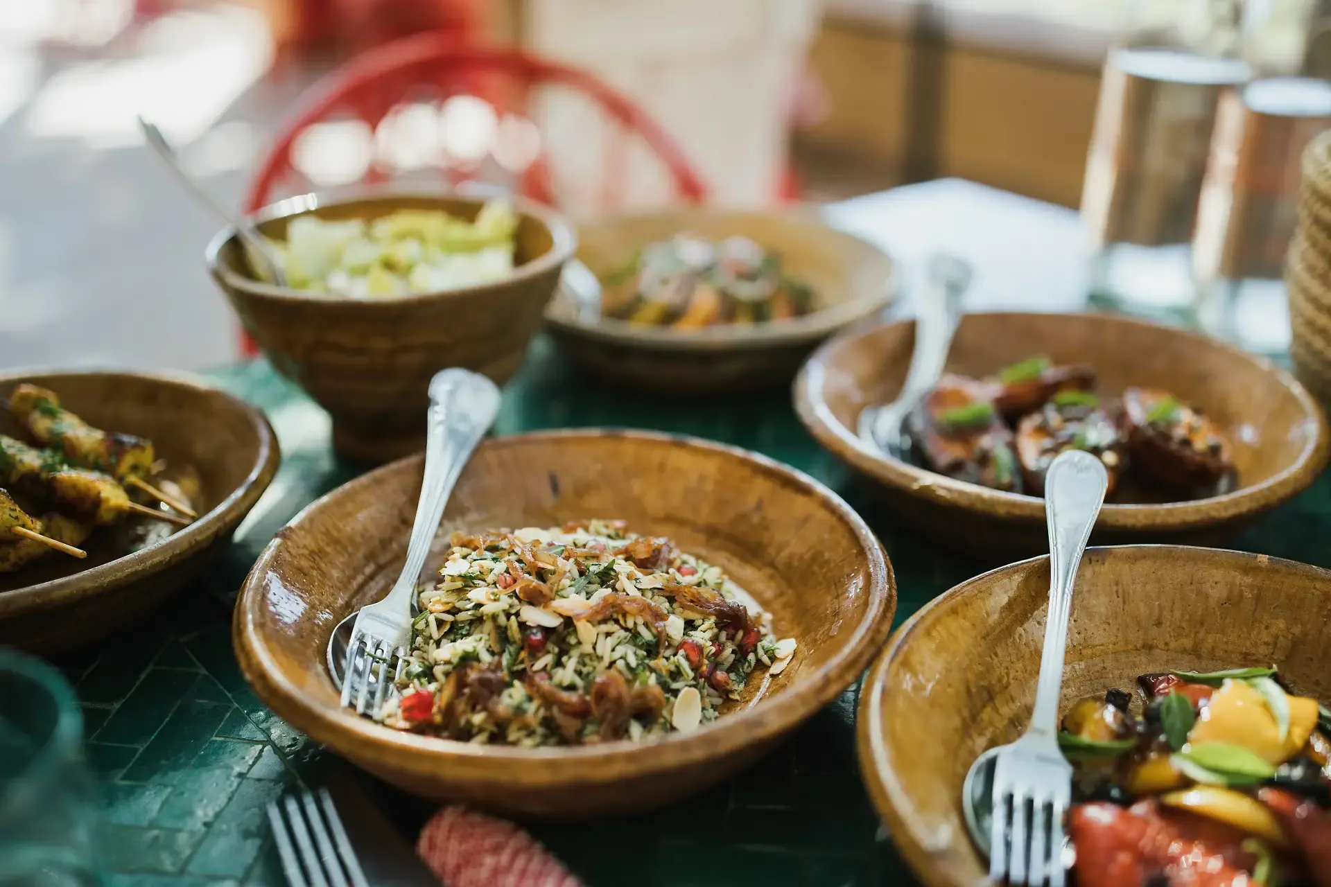 El Fenn, Africa — Wooden bowls of composed salads and grilled vegetables arranged on green table with silver forks, warm natural light.