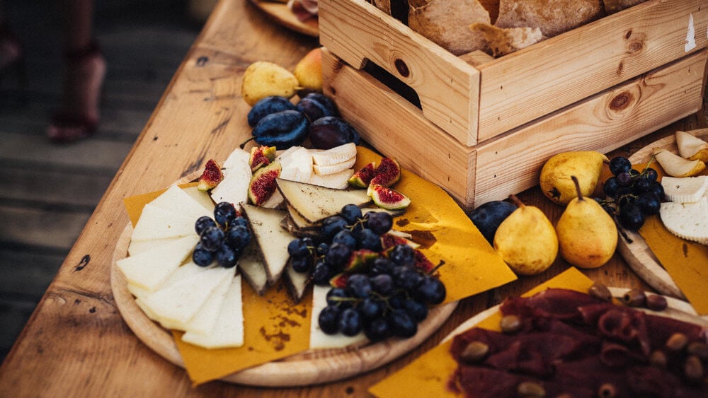 Villa Lena, Europe — Artisanal charcuterie board with aged cheese, dark grapes, fresh figs, and pears on wooden surface and crate, warm afternoon light.