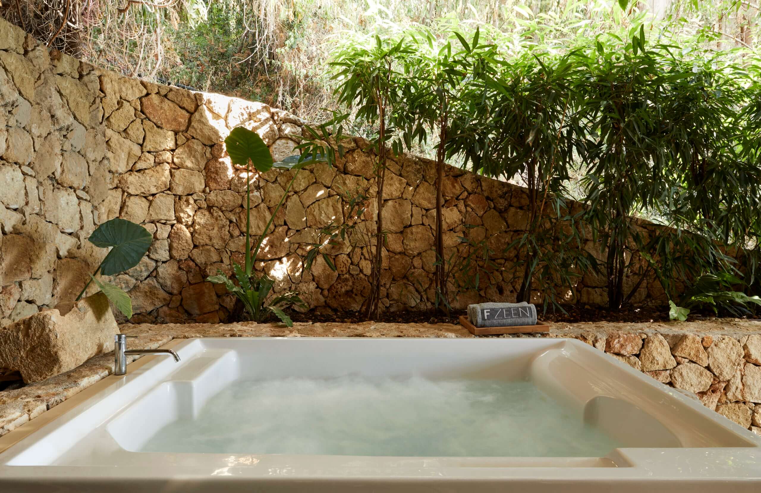 F Zeen Retreat, Europe — Soaking tub with mineral water set against weathered stone wall and lush greenery in spa bathroom.