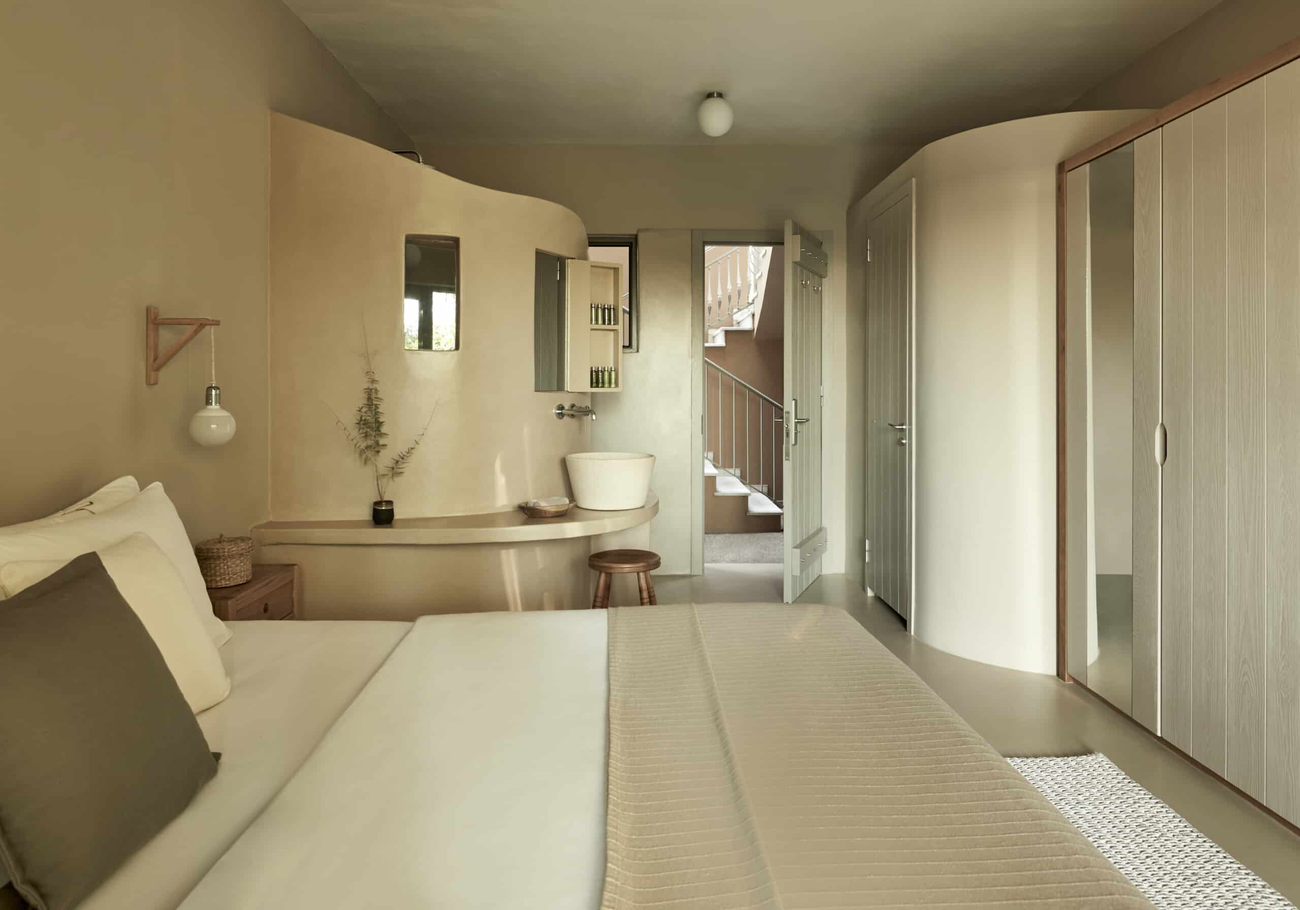 F Zeen Retreat, Europe — Minimalist bedroom with curved ensuite, natural light, neutral palette, wooden accents, and integrated spa bath with Japanese-inspired design elements.
